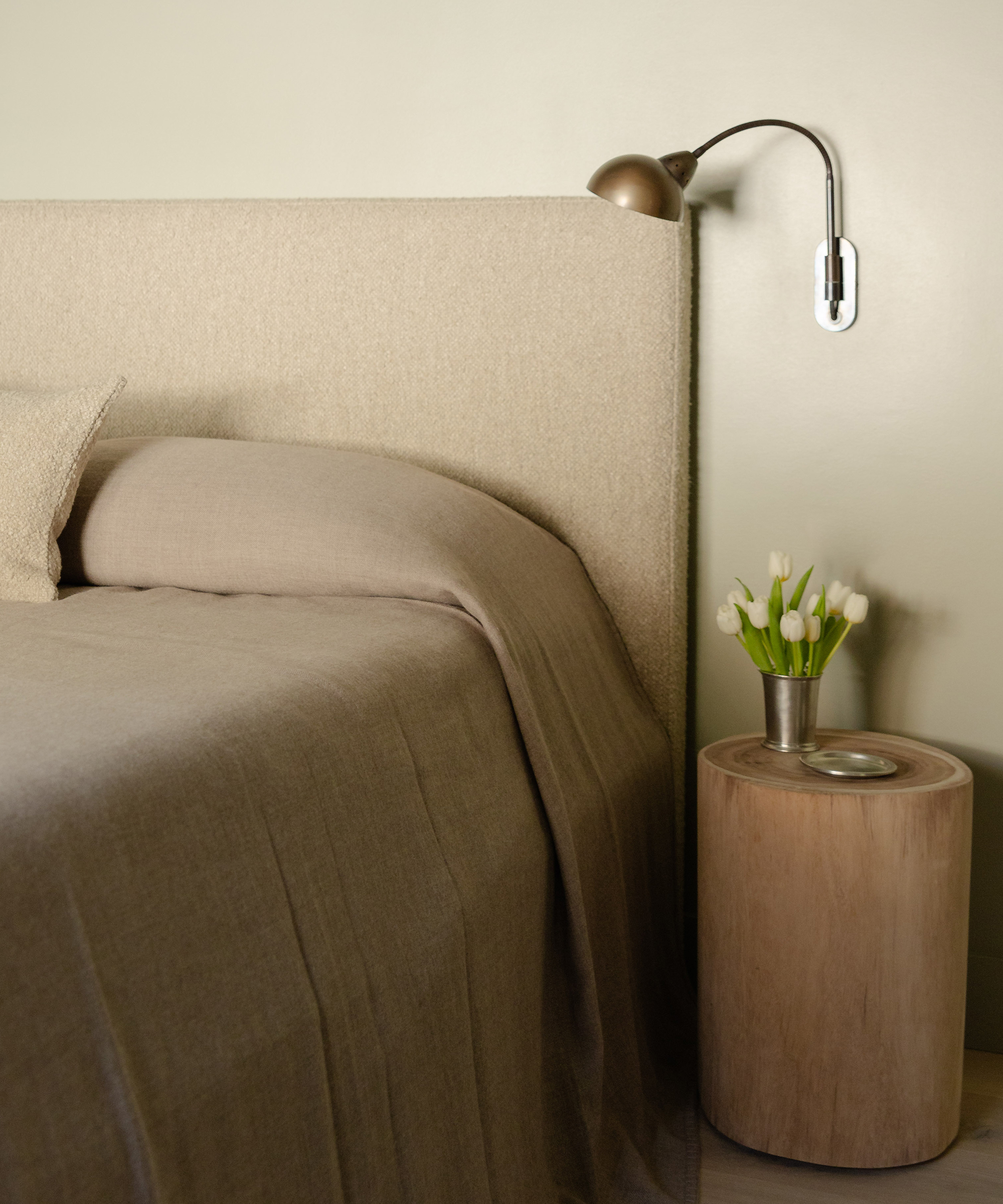 a primary bedroom with a boucle headboard and wooden nightstand with tulips in a silver vase