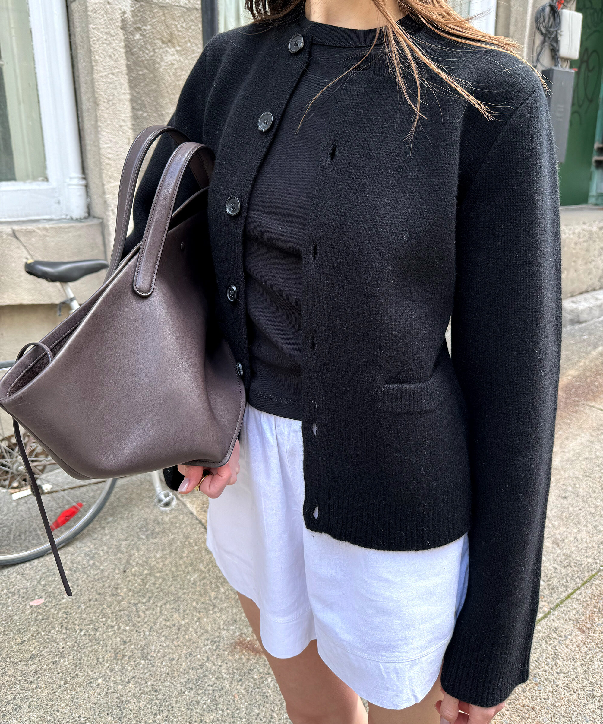 anna porte wearing white cotton shorts and a black cooper sweater with a leather tote