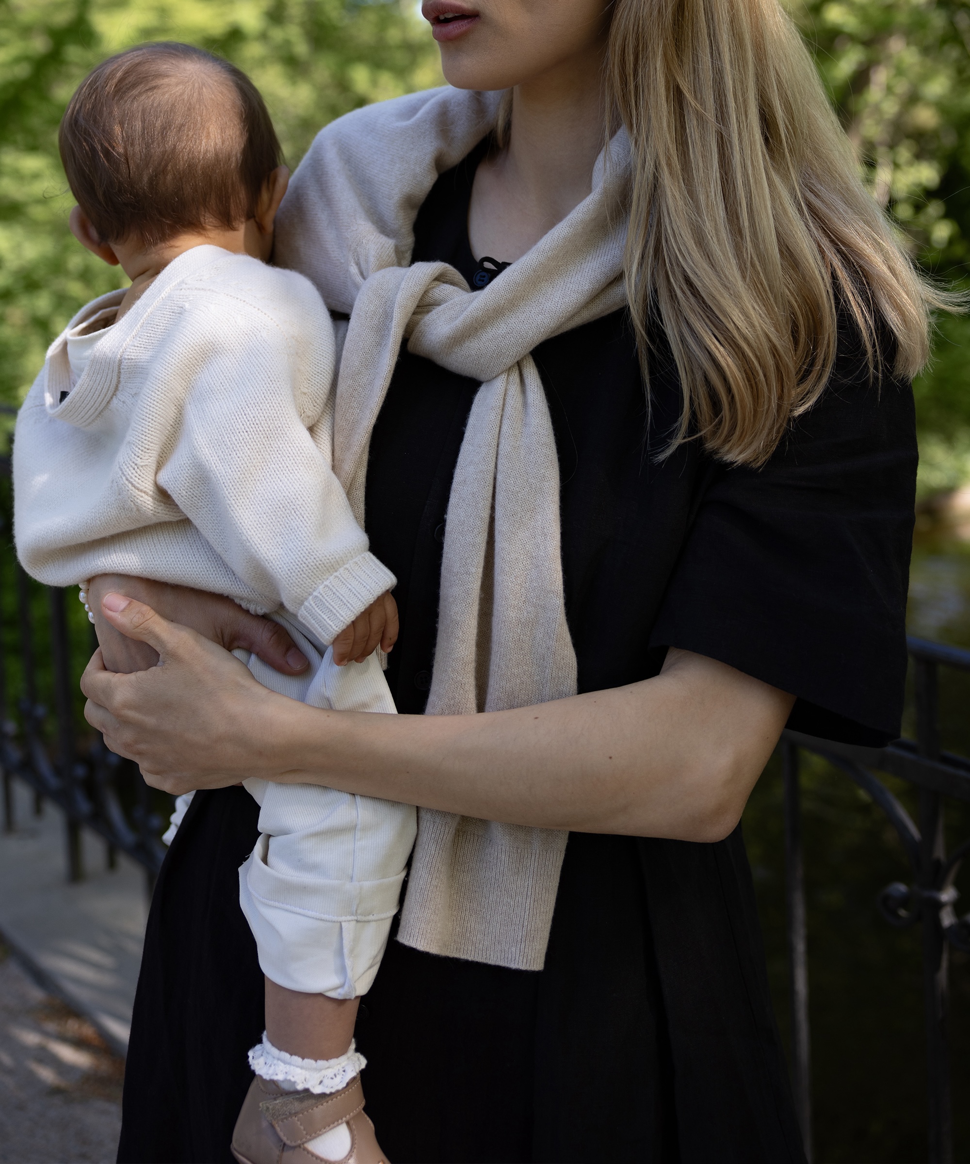 cecilie in a black dress wearing a sweater tied over her shoulders holding her baby in an ivory cardigan