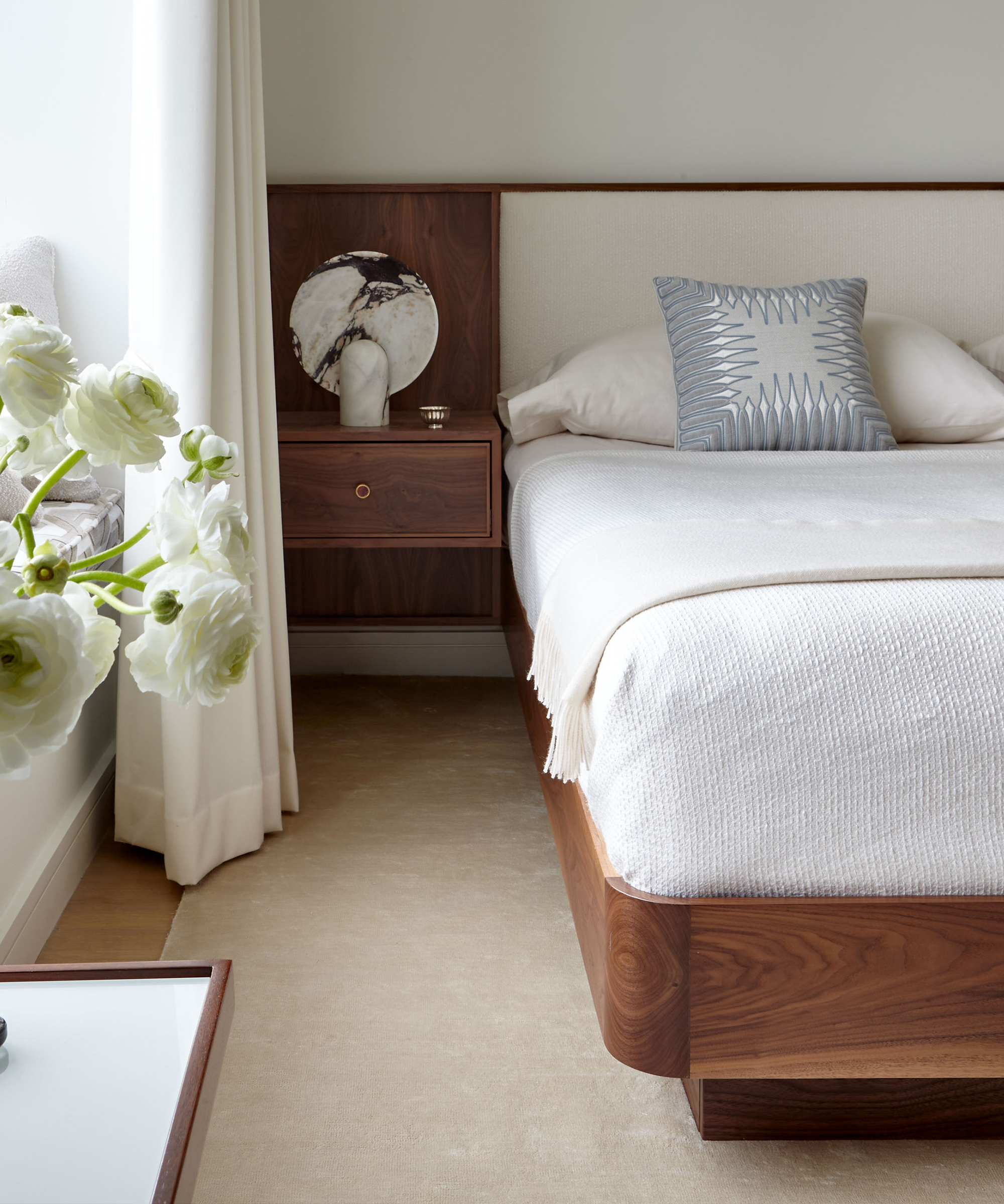 a bedroom with a wooden headboard and ivory bedding and a built in nightstand with a marble table lamp