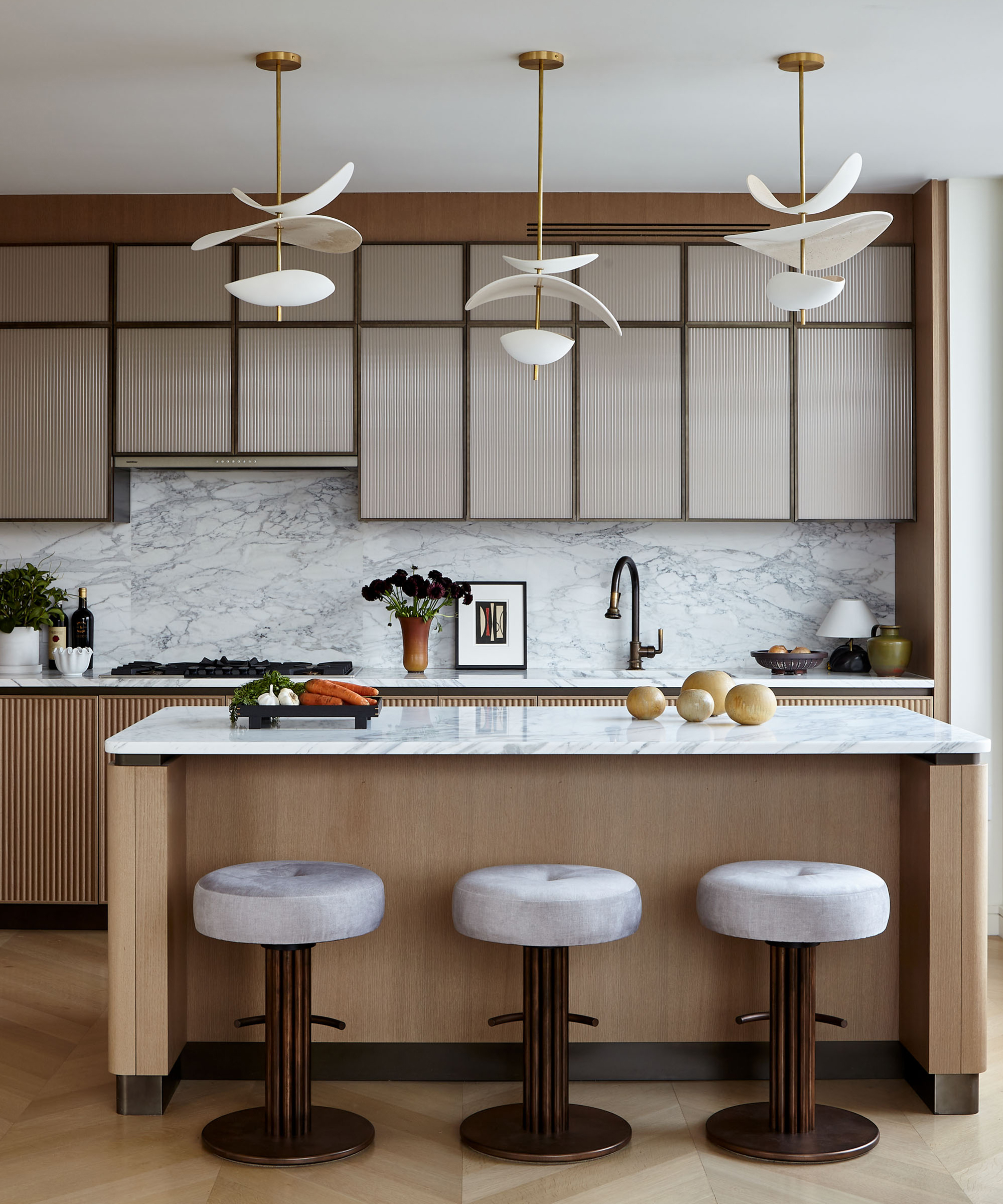 a brown kitchen with three counter stools and a wooden island with white marble counters