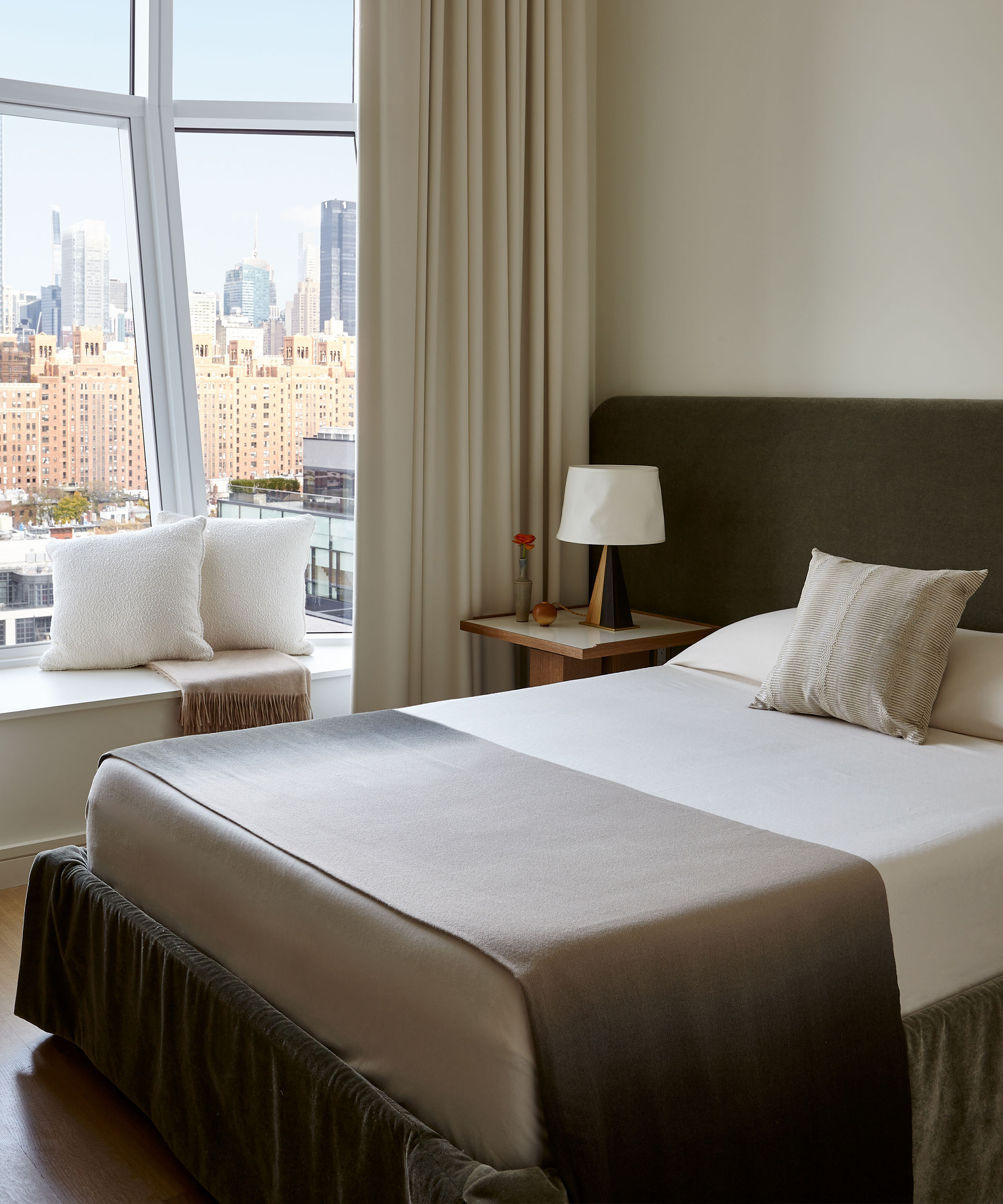 a bedroom with a large bay window and a green velvet headboard with a taupe blanket