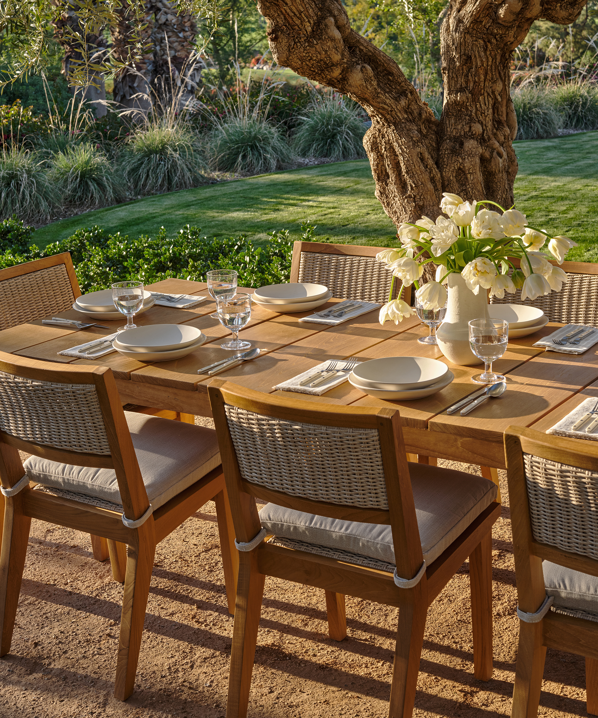 outdoor dining table with outdoor dining chairs and a table set with a vase of flowers and plates