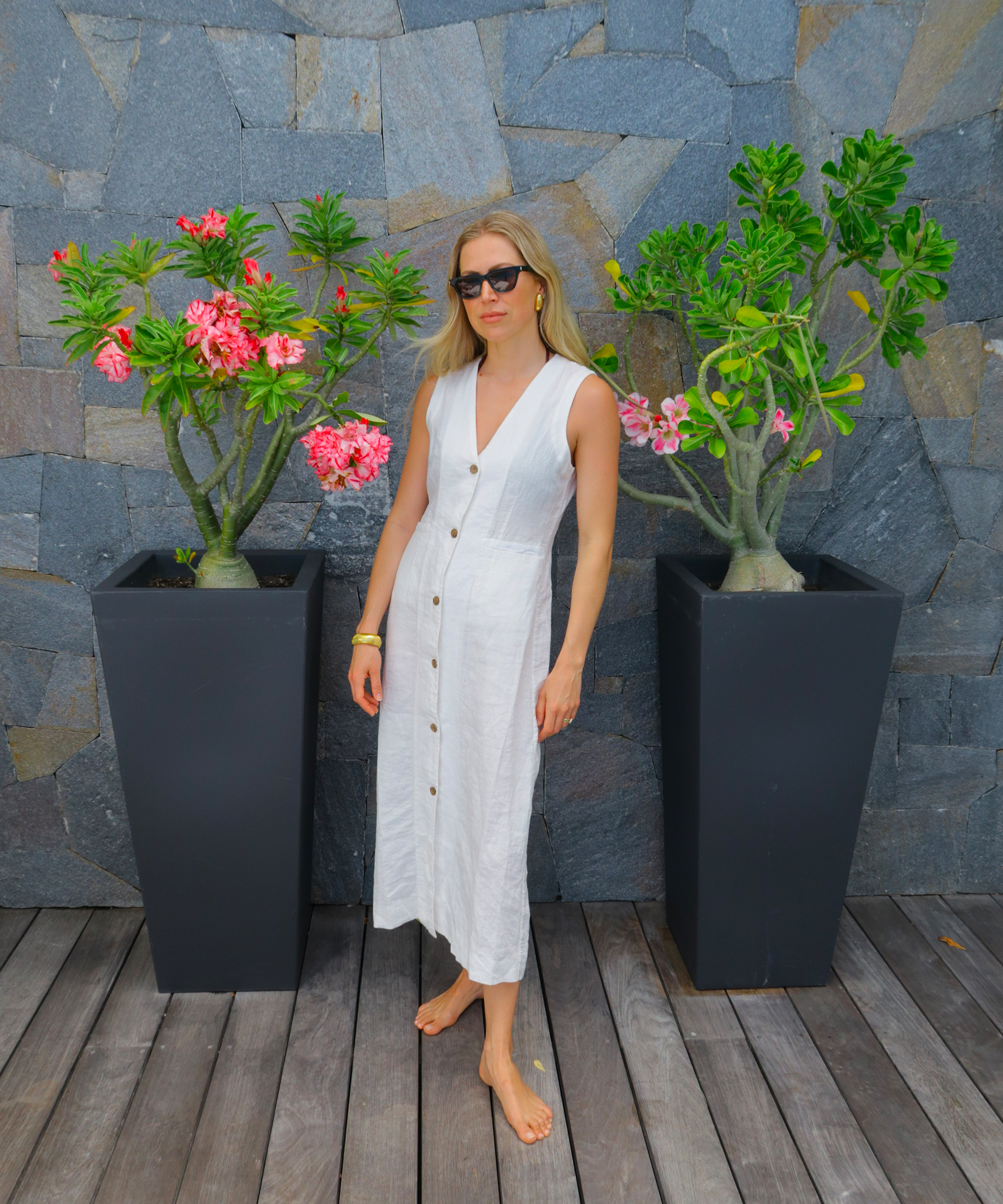 a white linen dress on a wooden deck with stone wall and planters