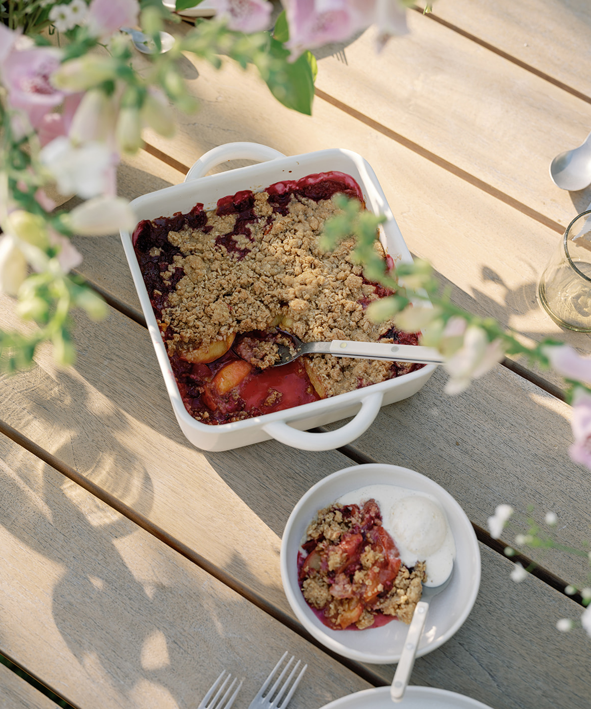 a berry crumble in a baking dish and a small bowl with ice cream and berries on a wooden dining table