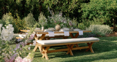an outdoor wooden dining table and dining bench with flowers and place settings in ivory