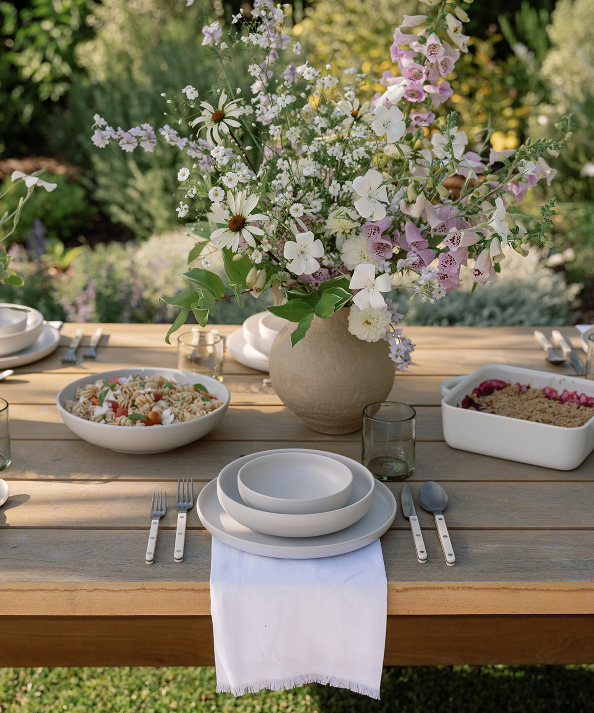 an outdoor wooden dining table with ivory dinnerware and a white linen napkin and two summer recipes