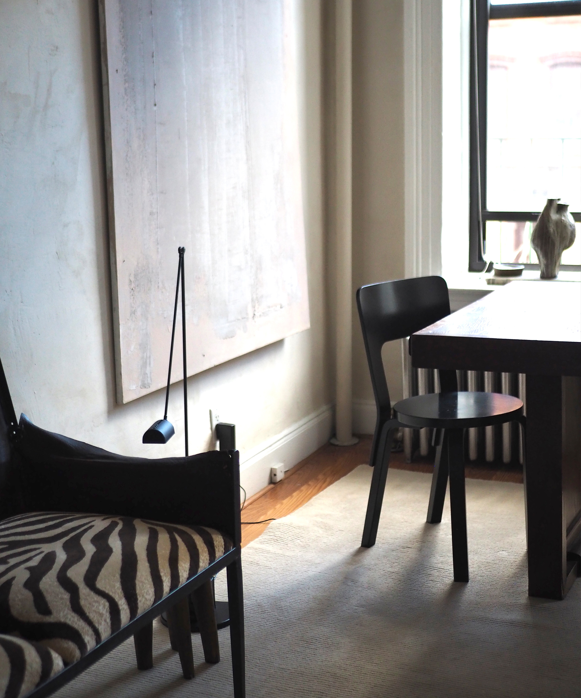 a wooden chair next to a wooden desk and a creme abstract painting hanging on a wall