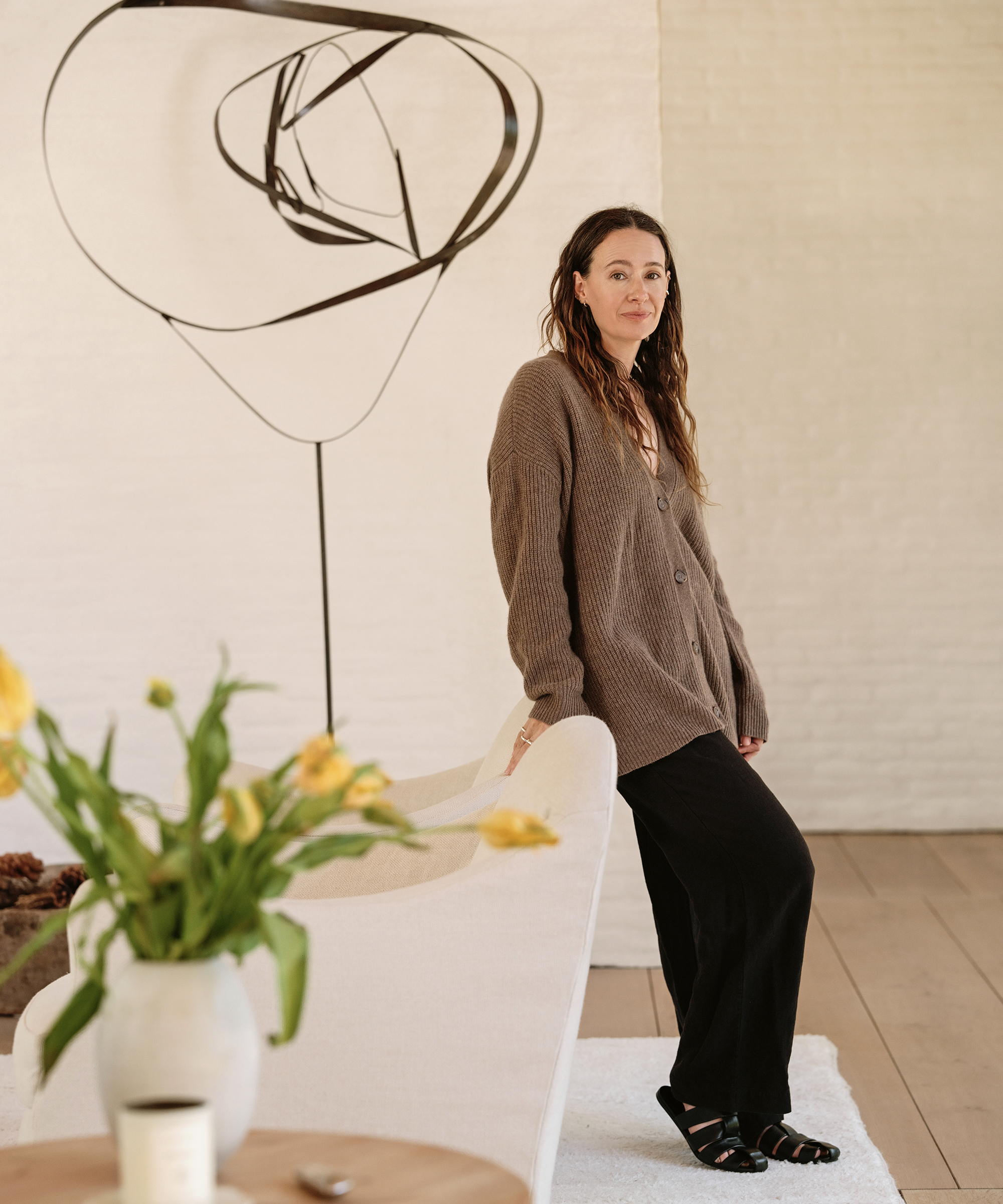 jenni wearing a taupe cashmere cocoon cardigan and black linen trousers with black mules standing in a living room