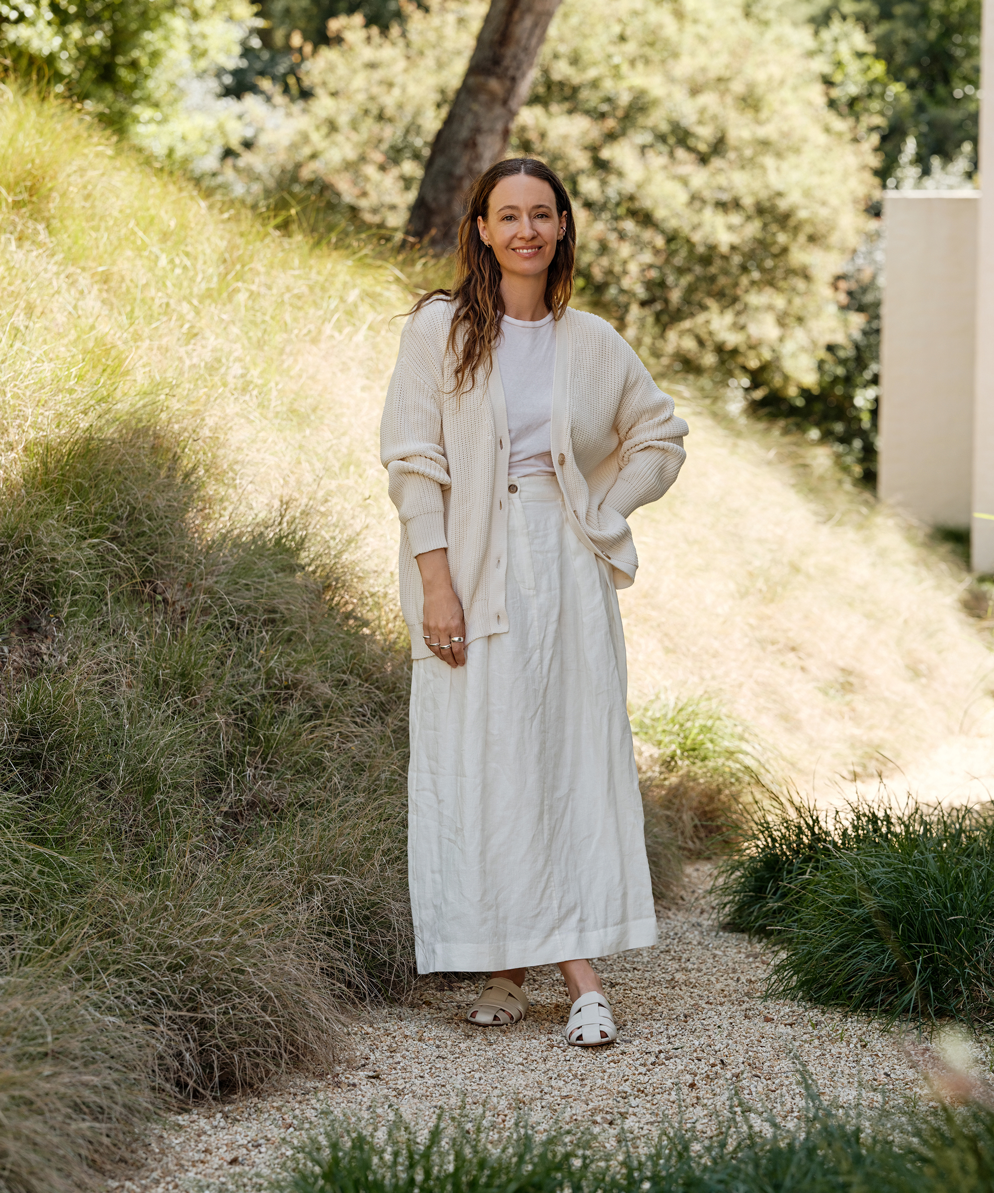jenni standing on a gravel path next to a hill of green grass wearing an ivory skirt and white tee with an ivory cardigan