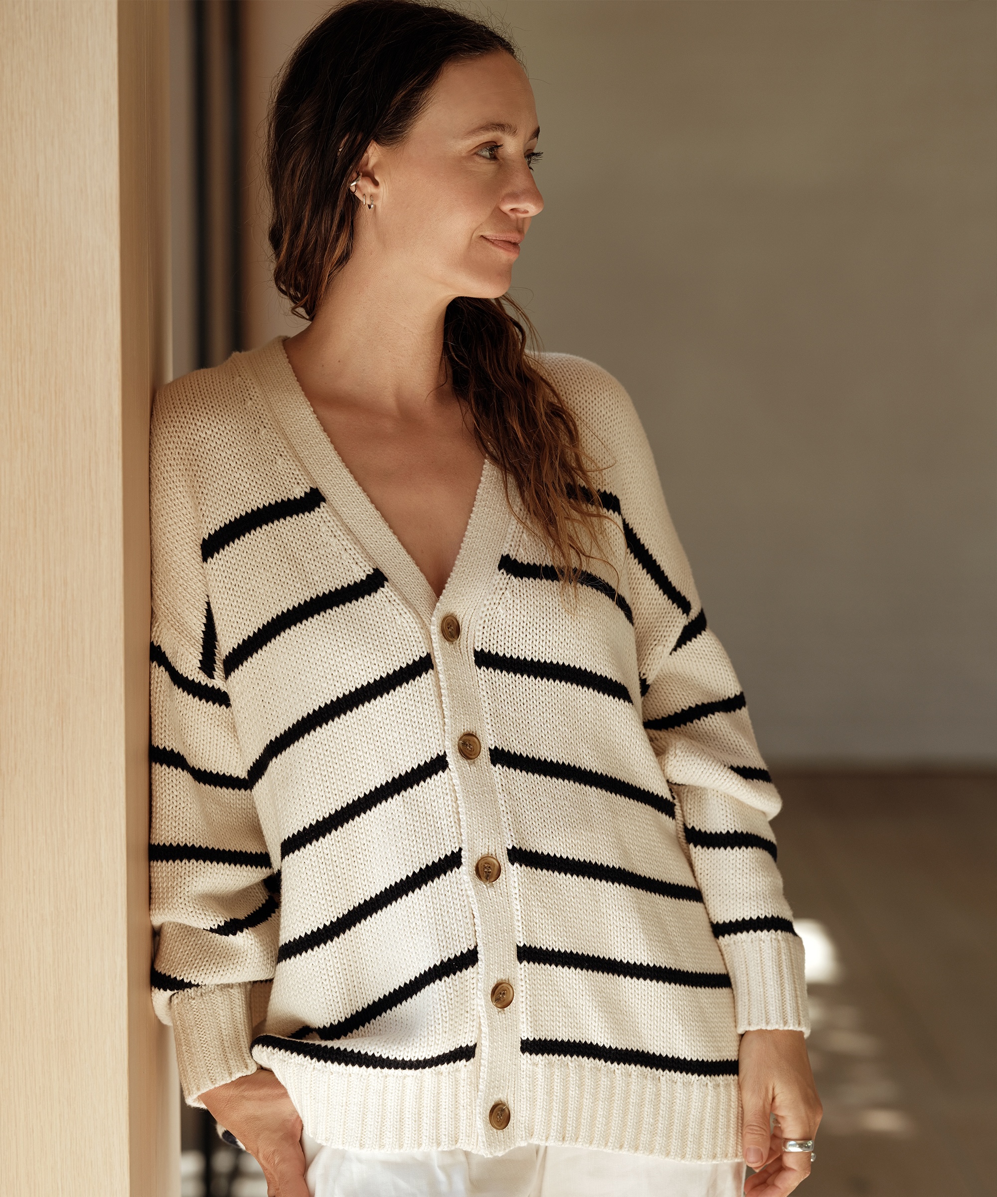 jenni leaning against a wall wearing a striped ivory and navy cardigan looking to the side