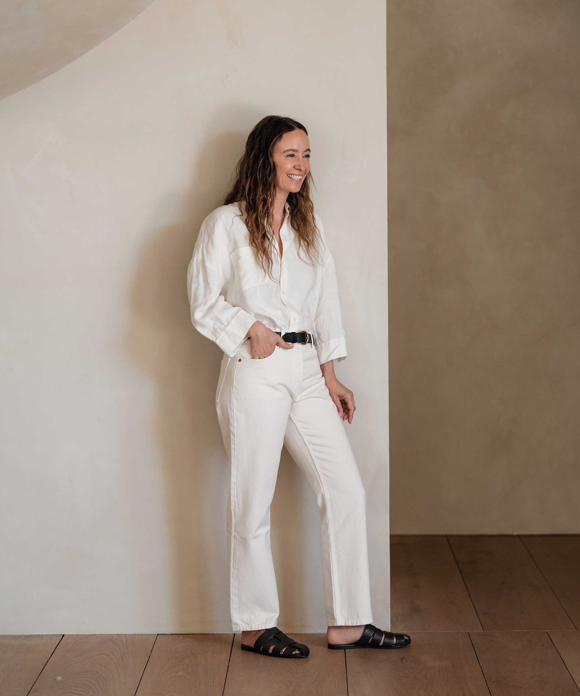 jenni in an ivory linen button down and ivory jeans with a brown belt and brown leather camilla mules