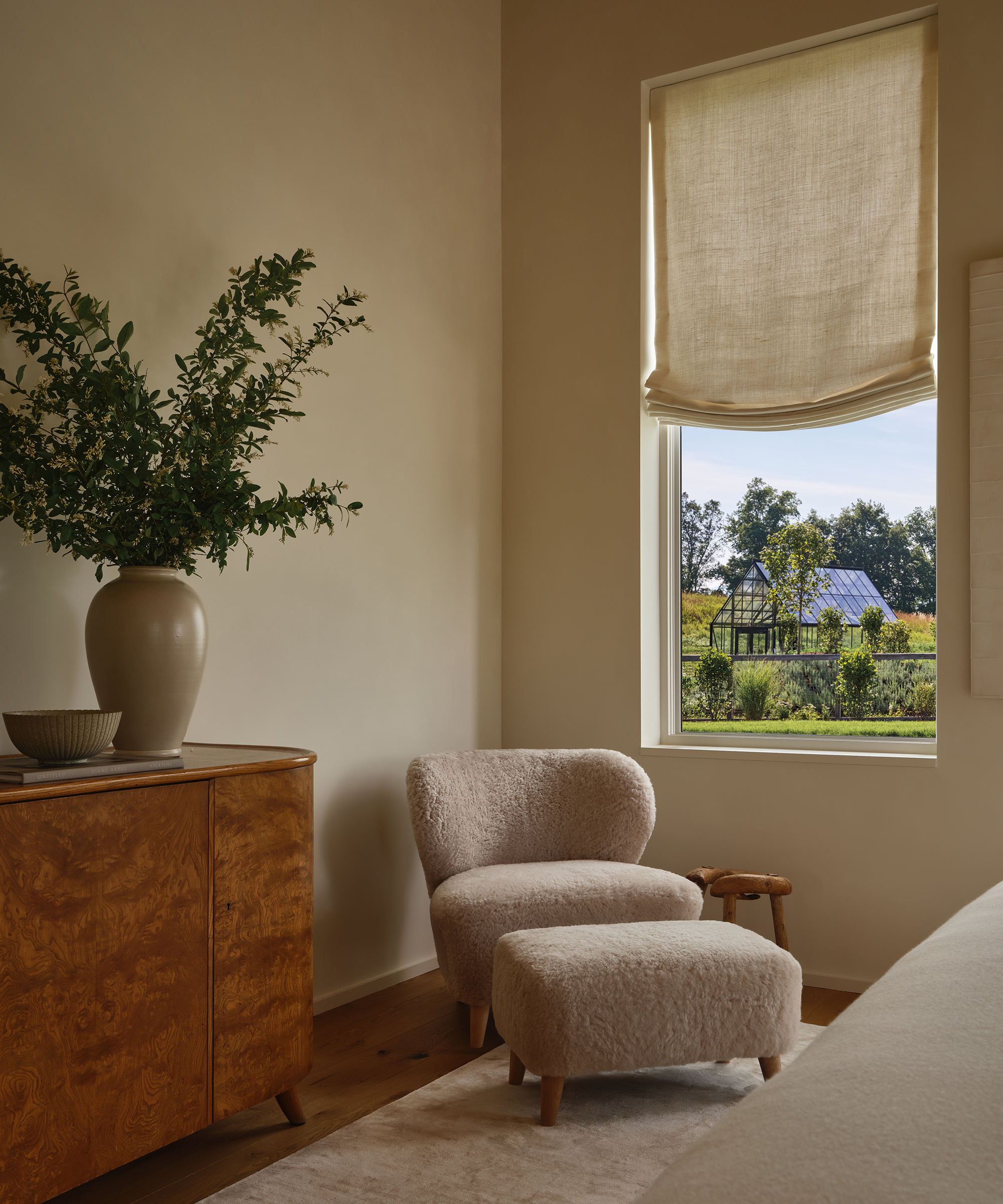 a guest bedroom with a shearling brentwood accent chair and shearling stool next to a burl antique chest with a vase of greenery