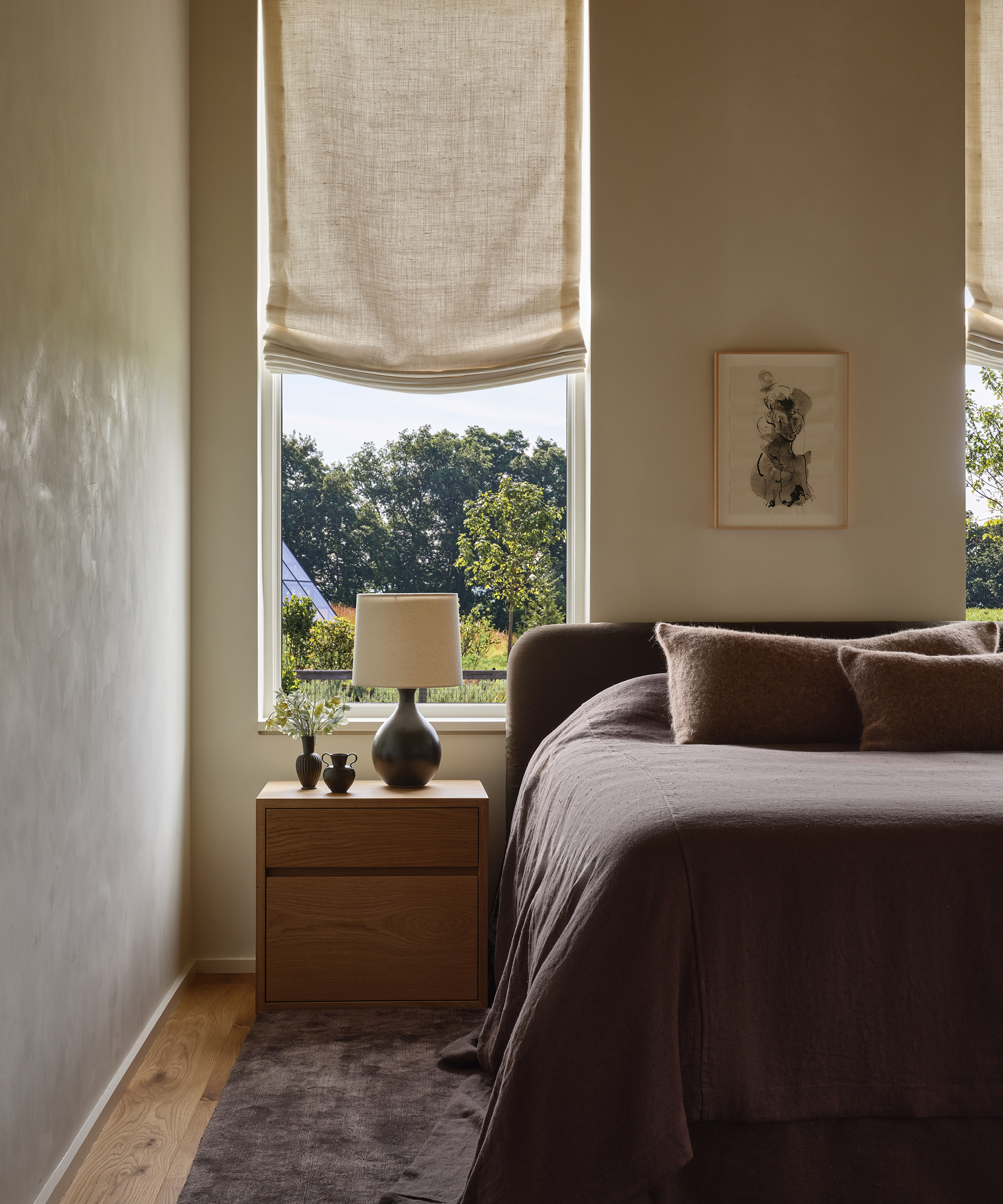 a guest bedroom with a brown headboard and a linen coverlet draped to the ground with a wooden nightstand