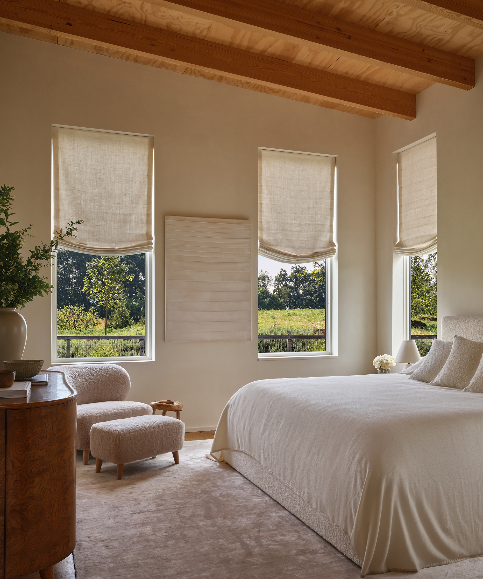a primary bedroom with an blush plush rug and an ivory boucle king headboard with a shearling brentwood chair