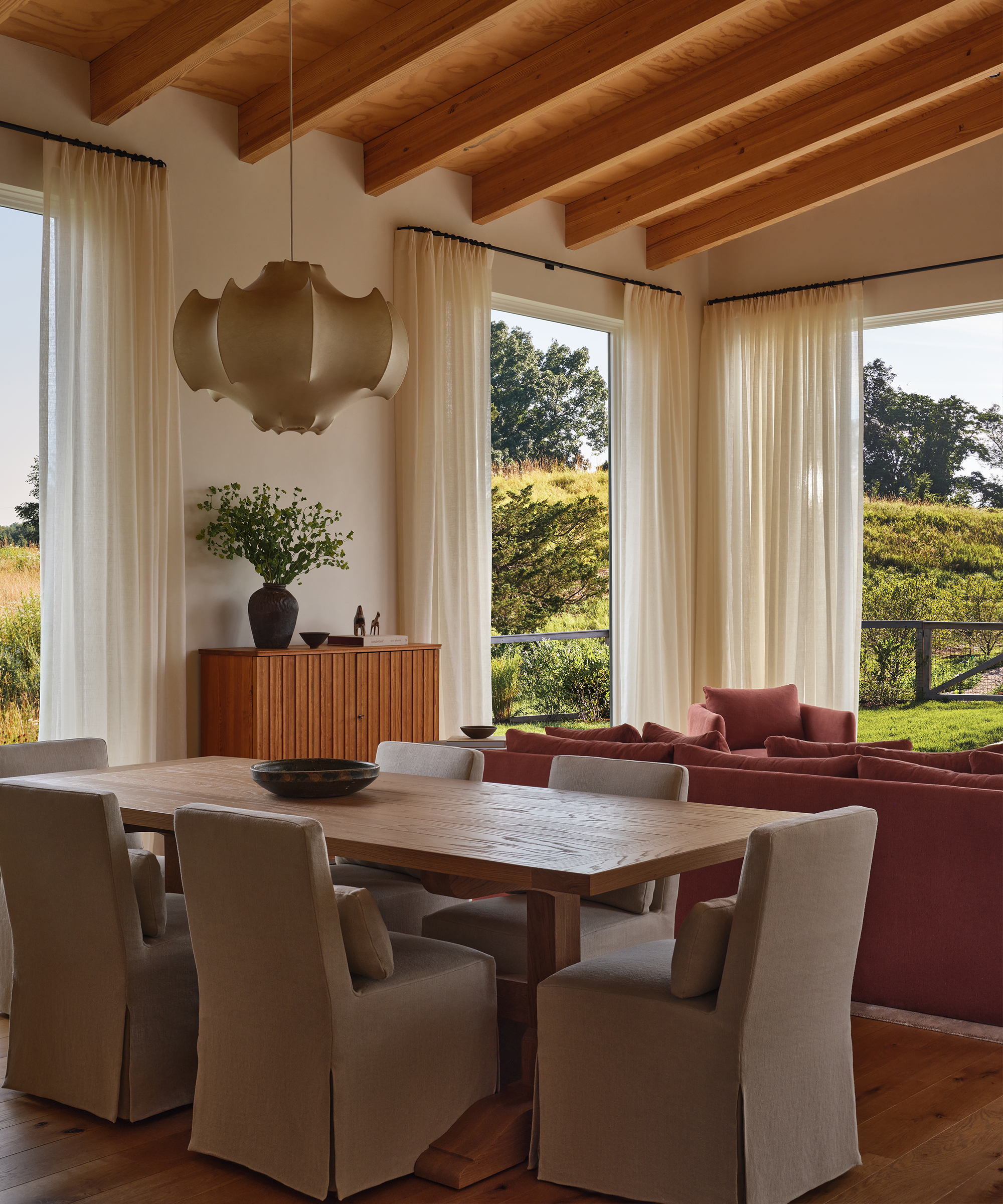 a great room with a wooden dining table and taupe slipcovered dining chairs next to the living room