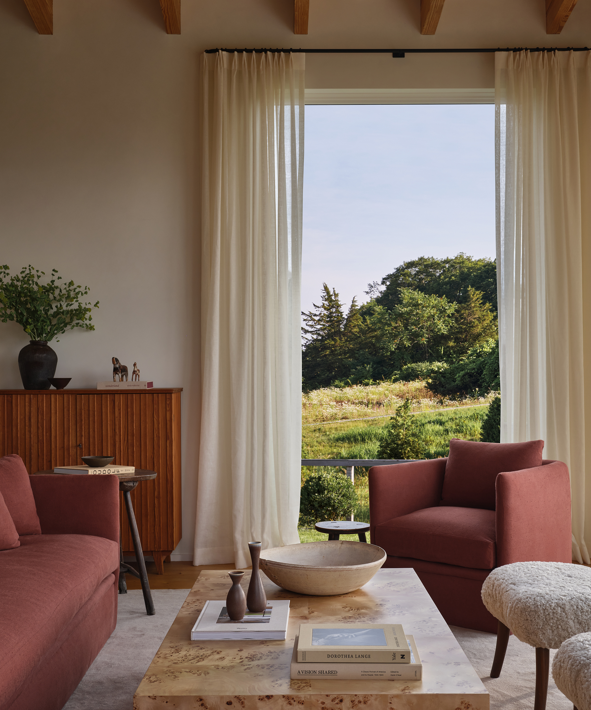 a living room with a red accent chair and a burlwood coffee table in front on a floor to ceiling window