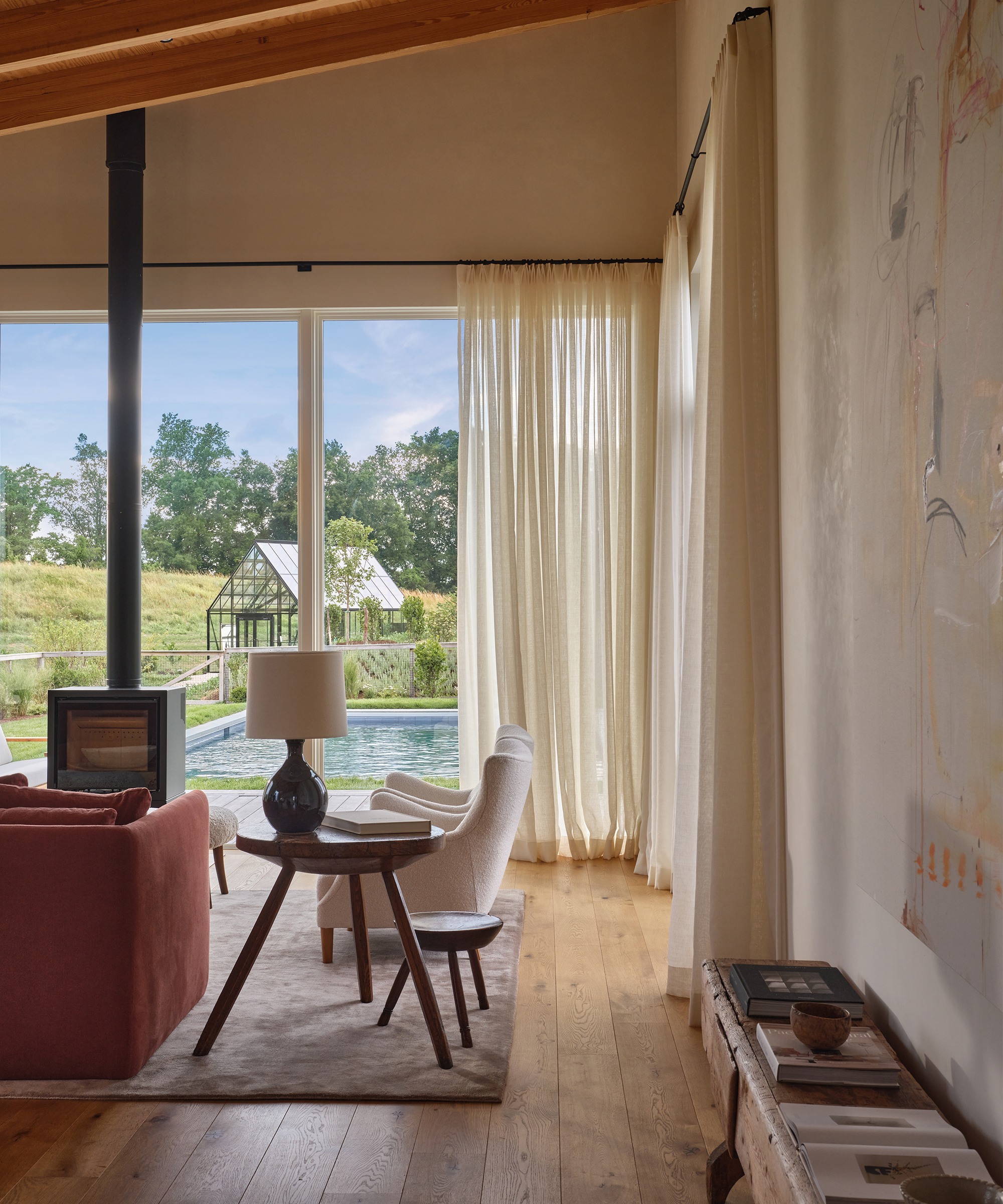 a living room with two sherpa accent chairs and creme curtains facing the backyard with a pool