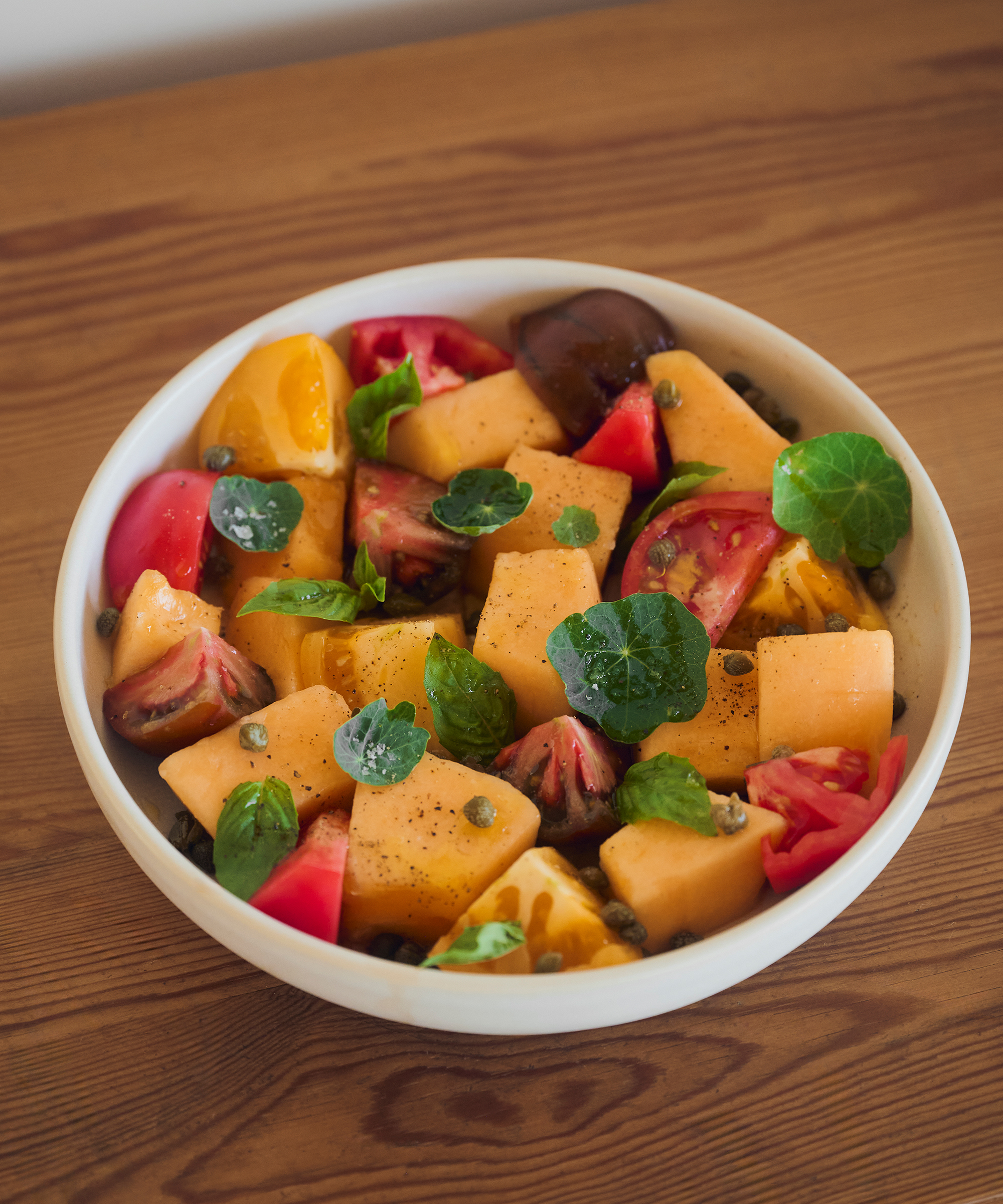 a bowl of melons and tomatoes on a wooden table