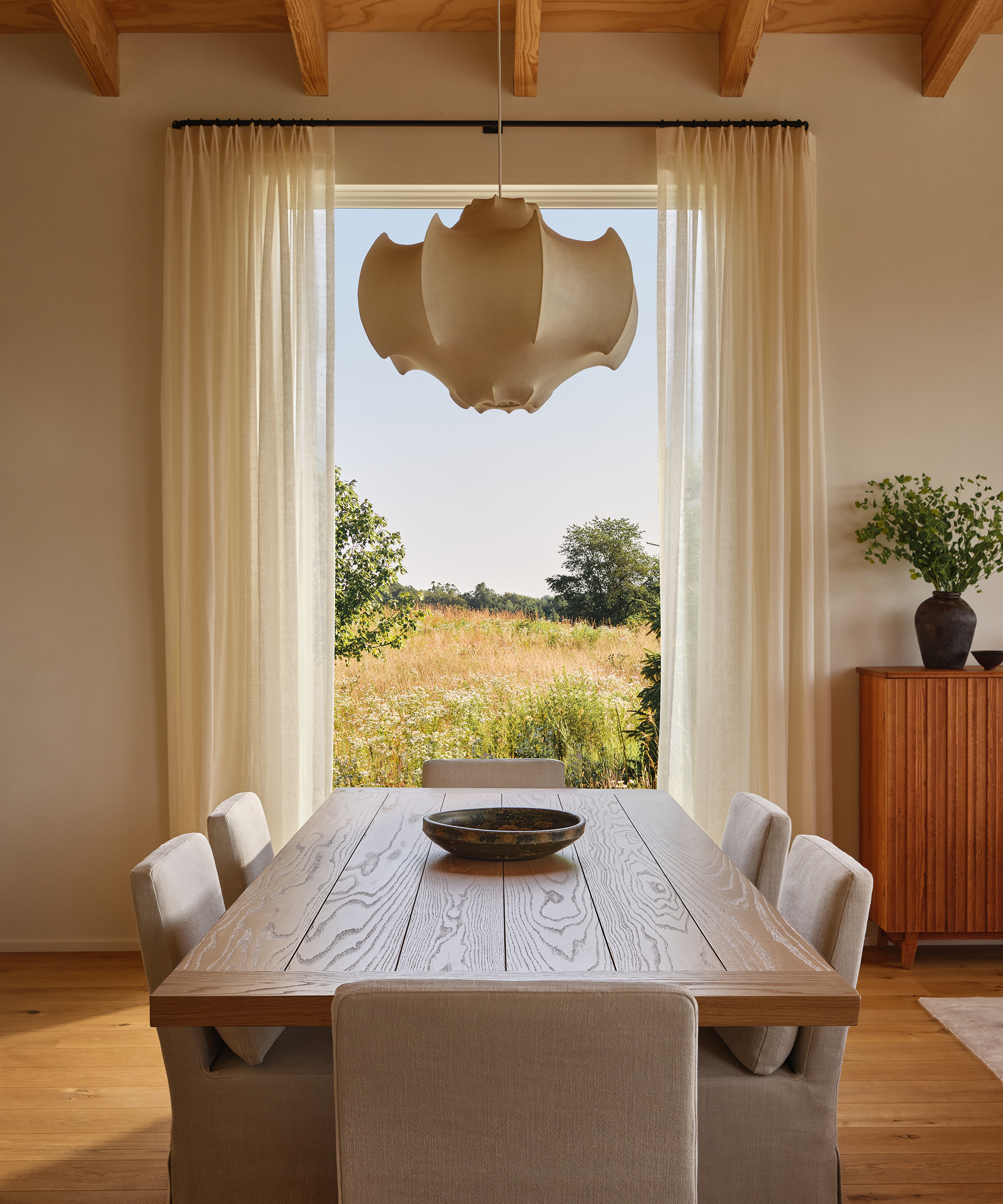 a dining room with taupe linen sunset dining chairs a wooden dining table and noguchi lamp