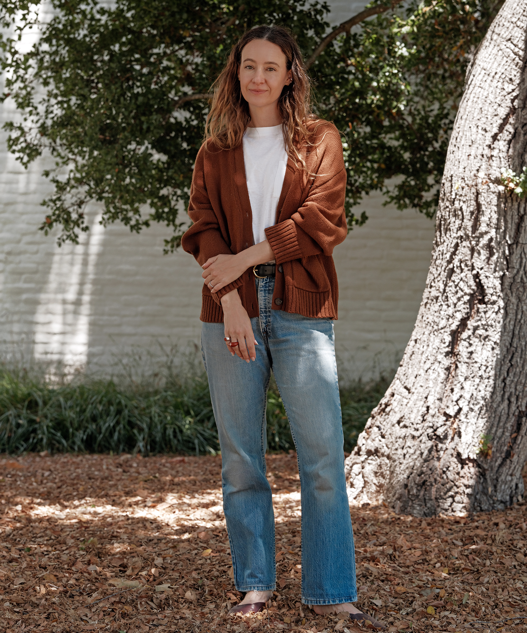 jenni wearing a vintage pocket tee and rust colored cardigan with denim outside under a green tree