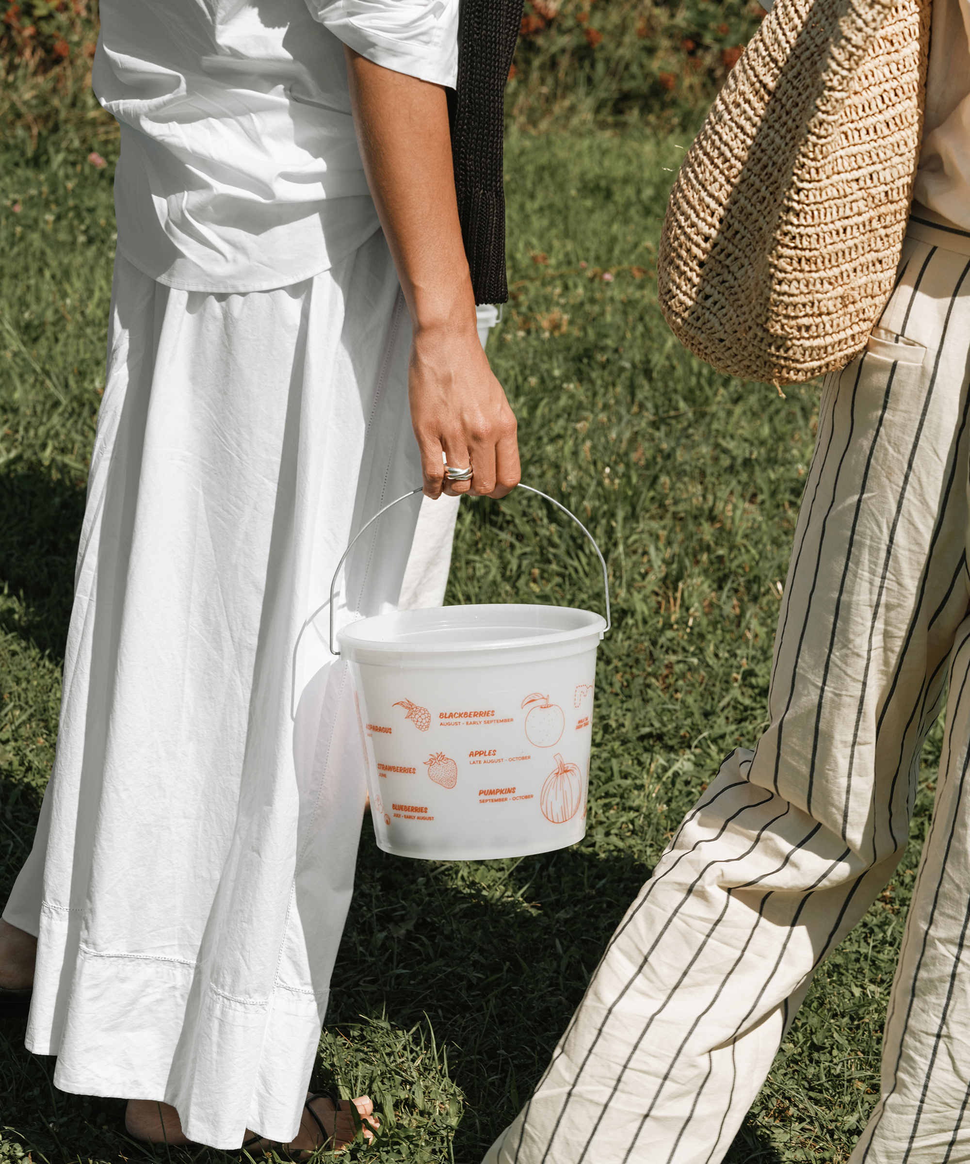 two women walking in a field holding a bucket of berries