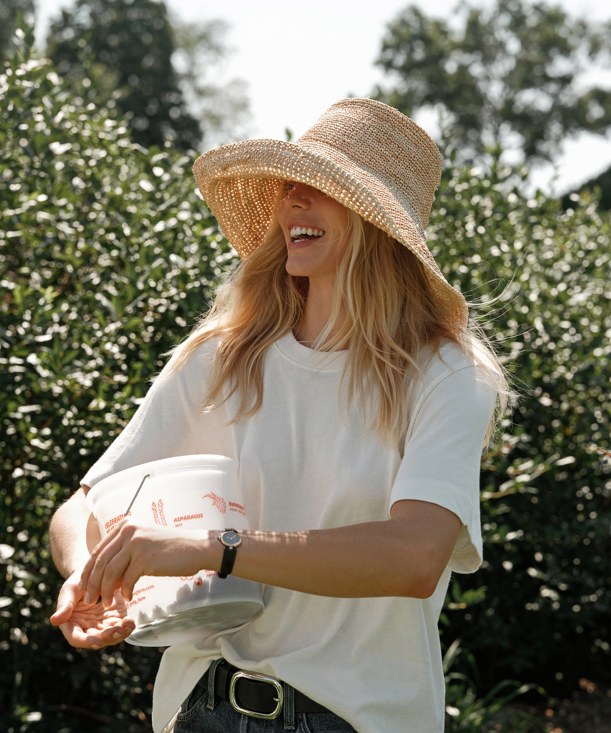 a woman with blonde hair wearing a white tshirt holding a bucket of berries