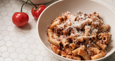 a bowl of pasta bolognese on a white tile counter next to tomatoes