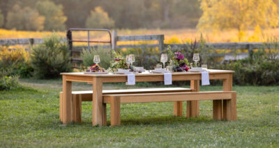 an outdoor wooden dining table set in a field with place settings
