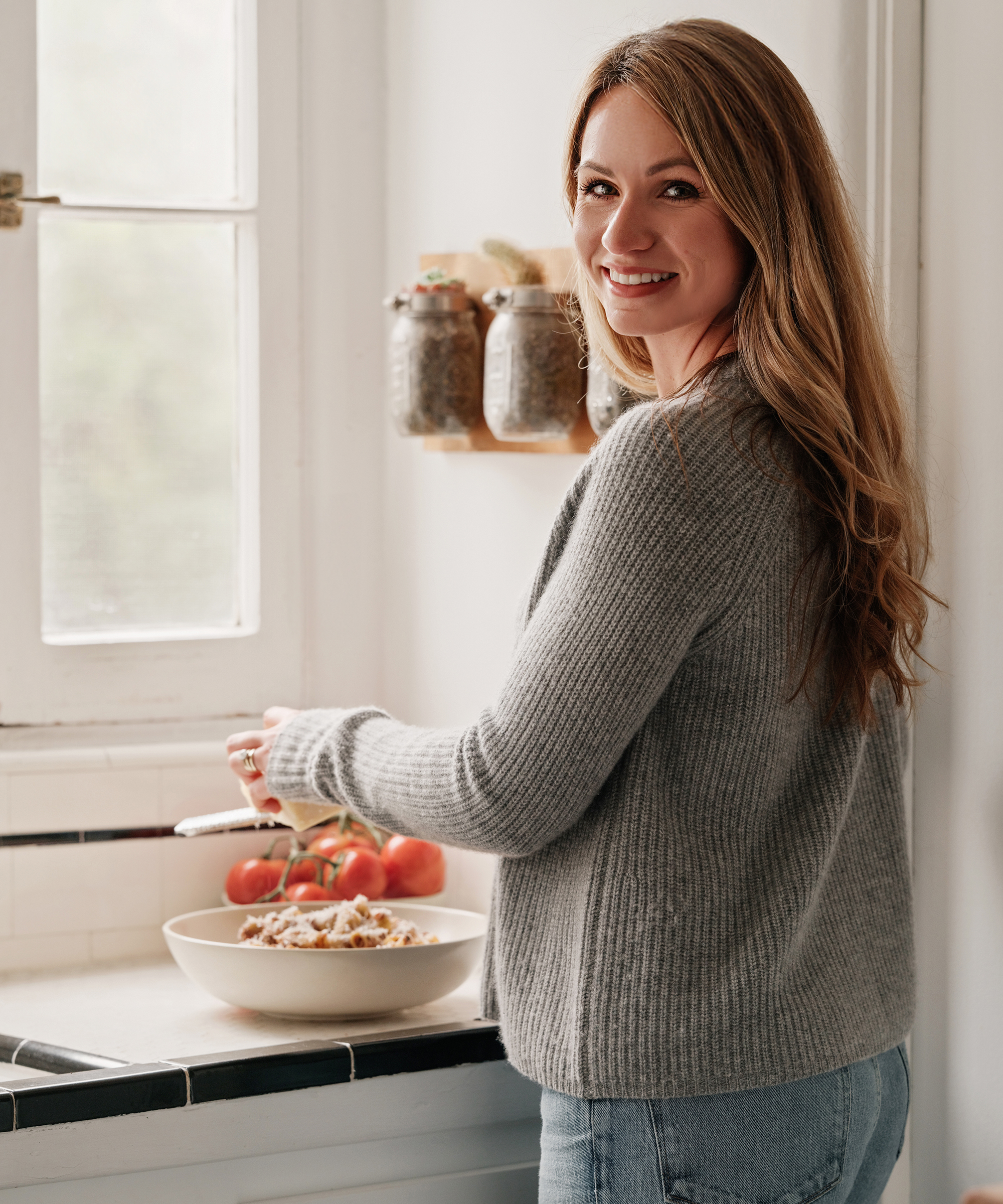 a portrait of a woman wearing a grey cashmere sweater in a white kitchen