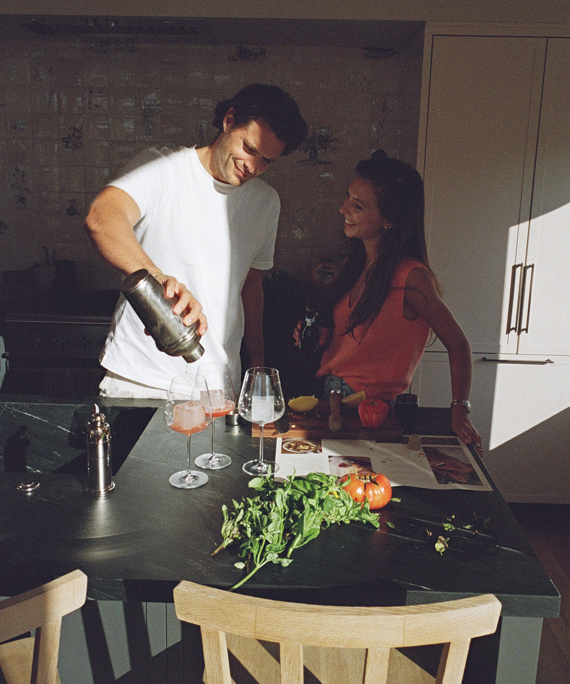 a man and a woman in a kitchen with a black countertop making cocktails