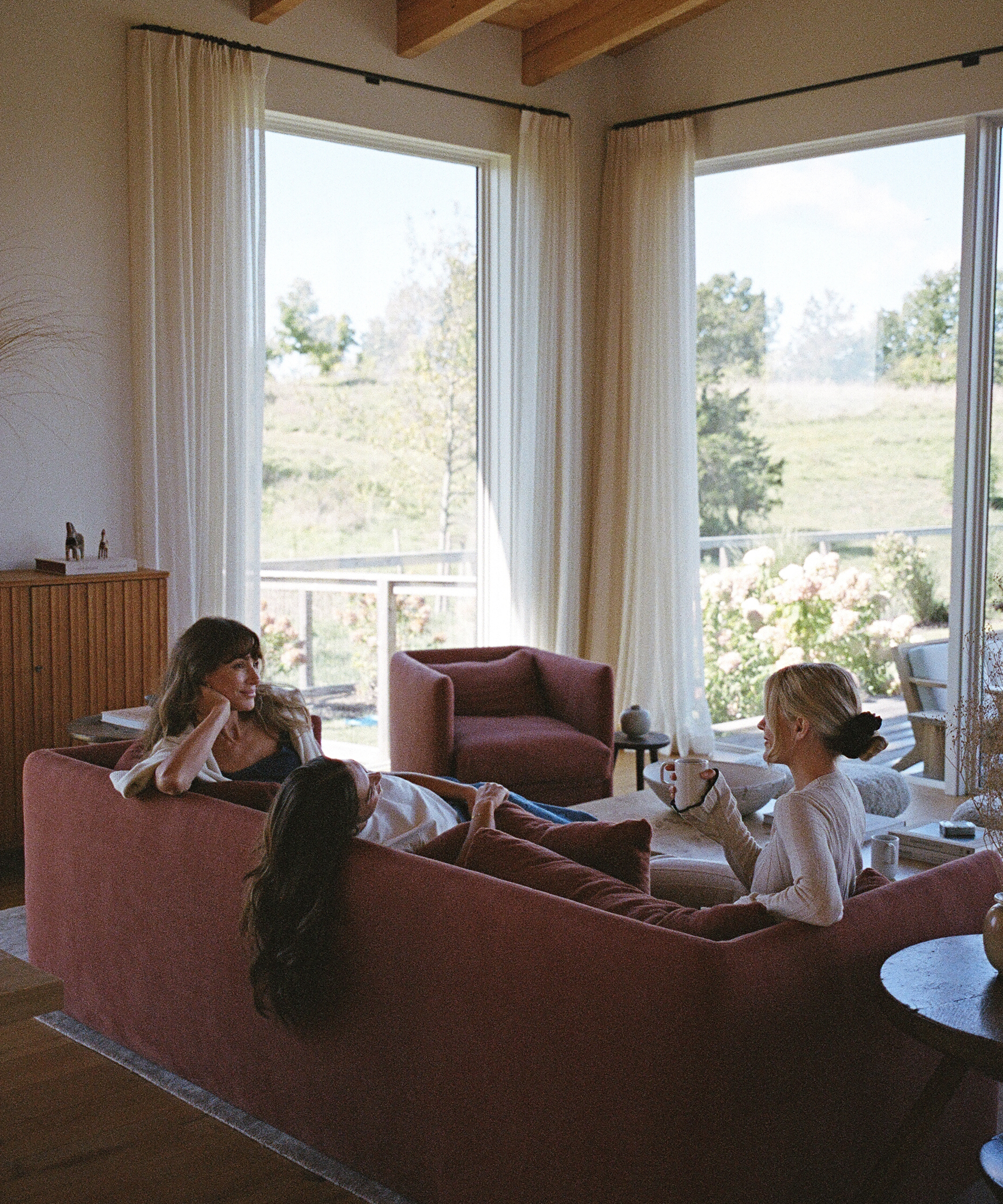a living room with a red couch and red accent chair with three women sitting on the couch