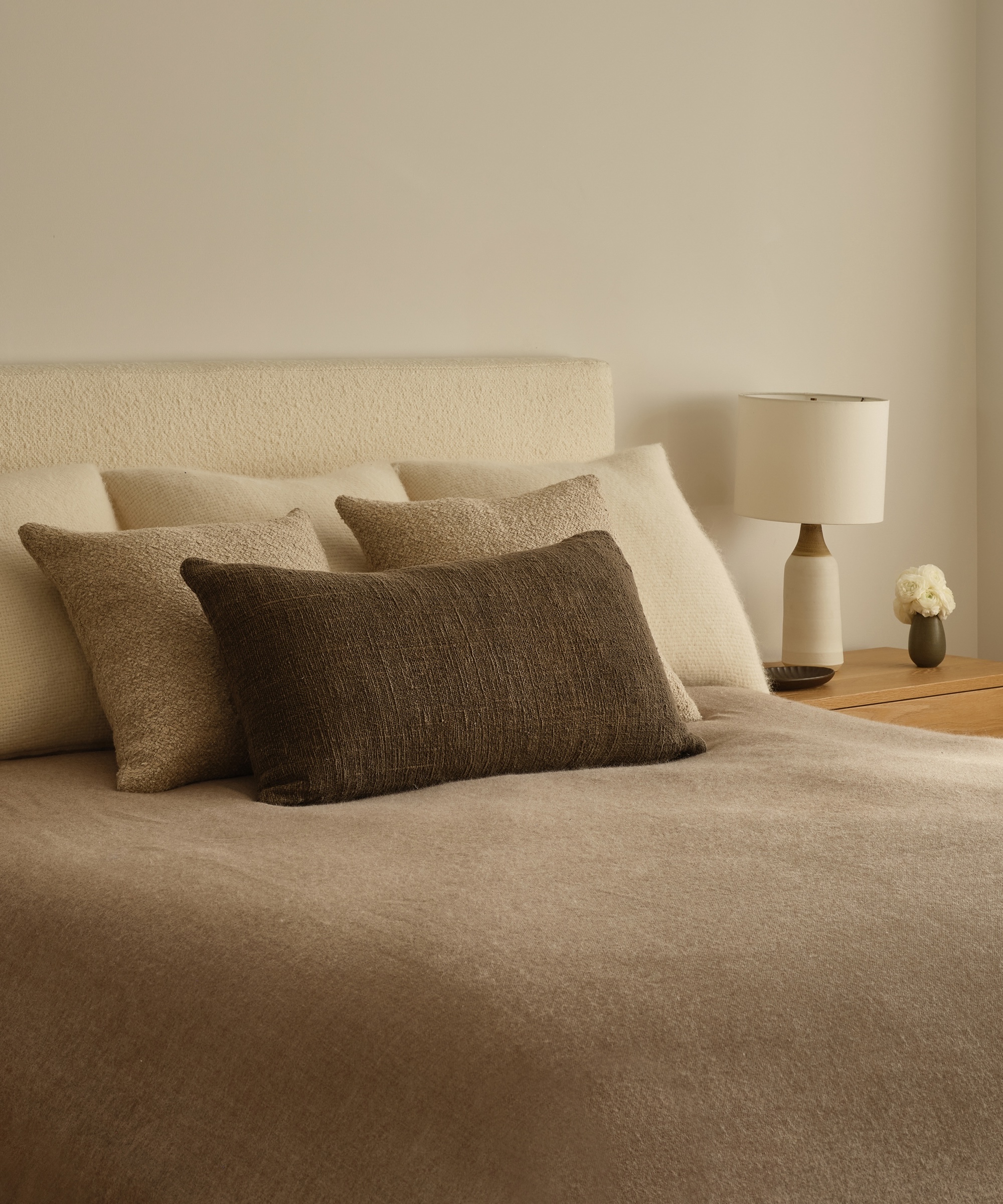 an ivory boucle bed with accent pillows and a charcoal lumbar pillow