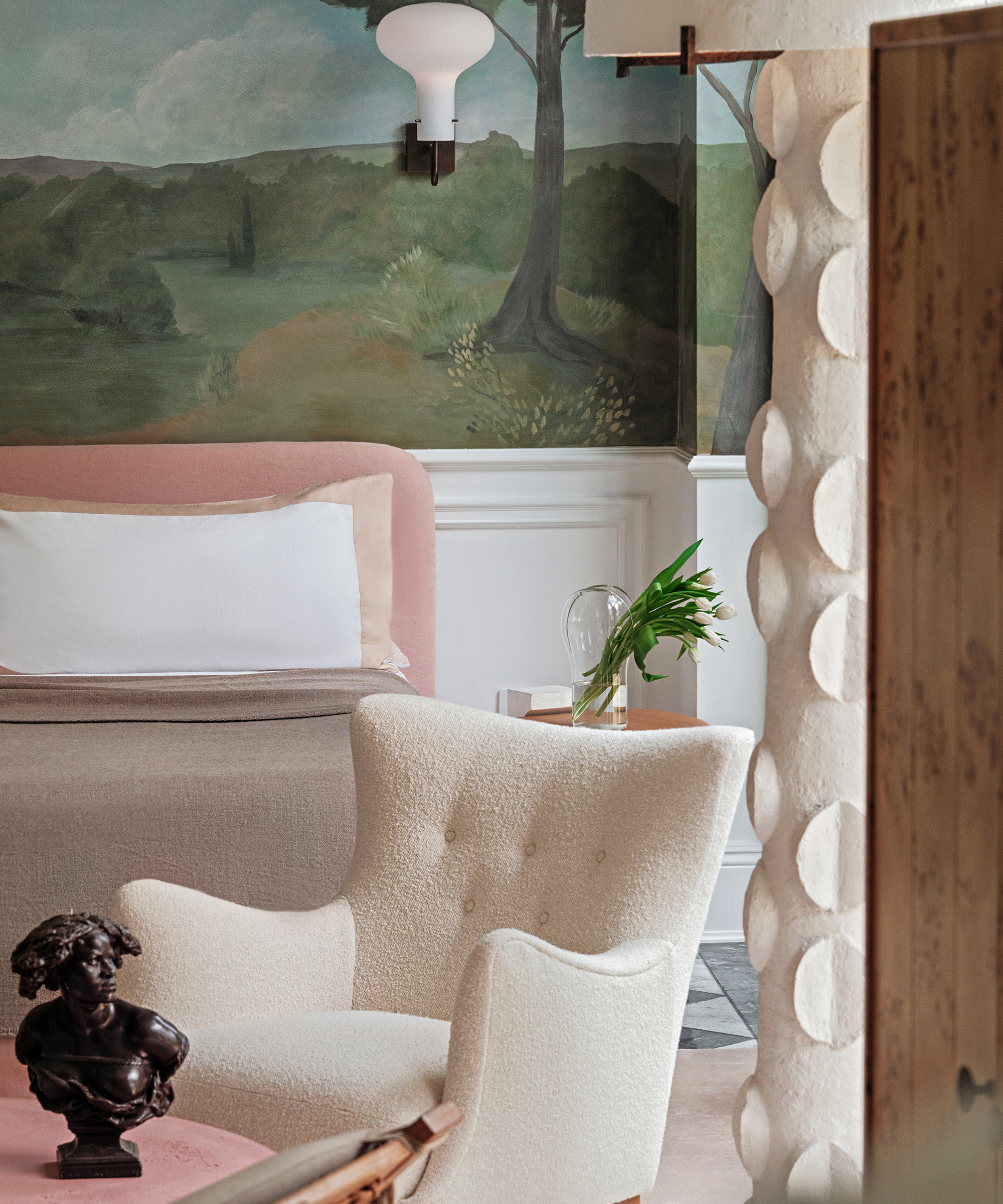 a bedroom with a boucle accent chair and painted mural wall