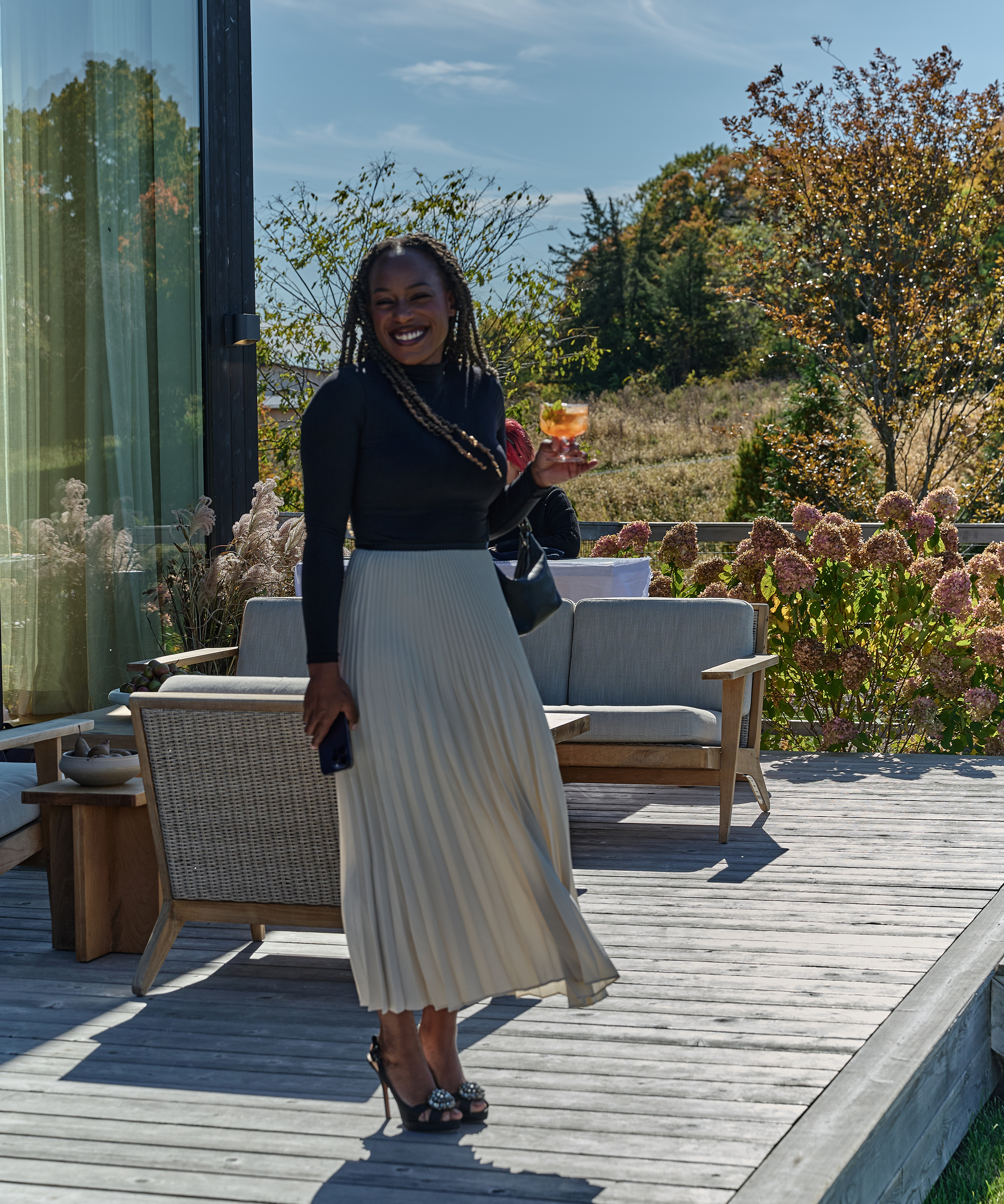 a guest standing outside wearing an ivory pleated skirt a black long sleeve tee and black heels