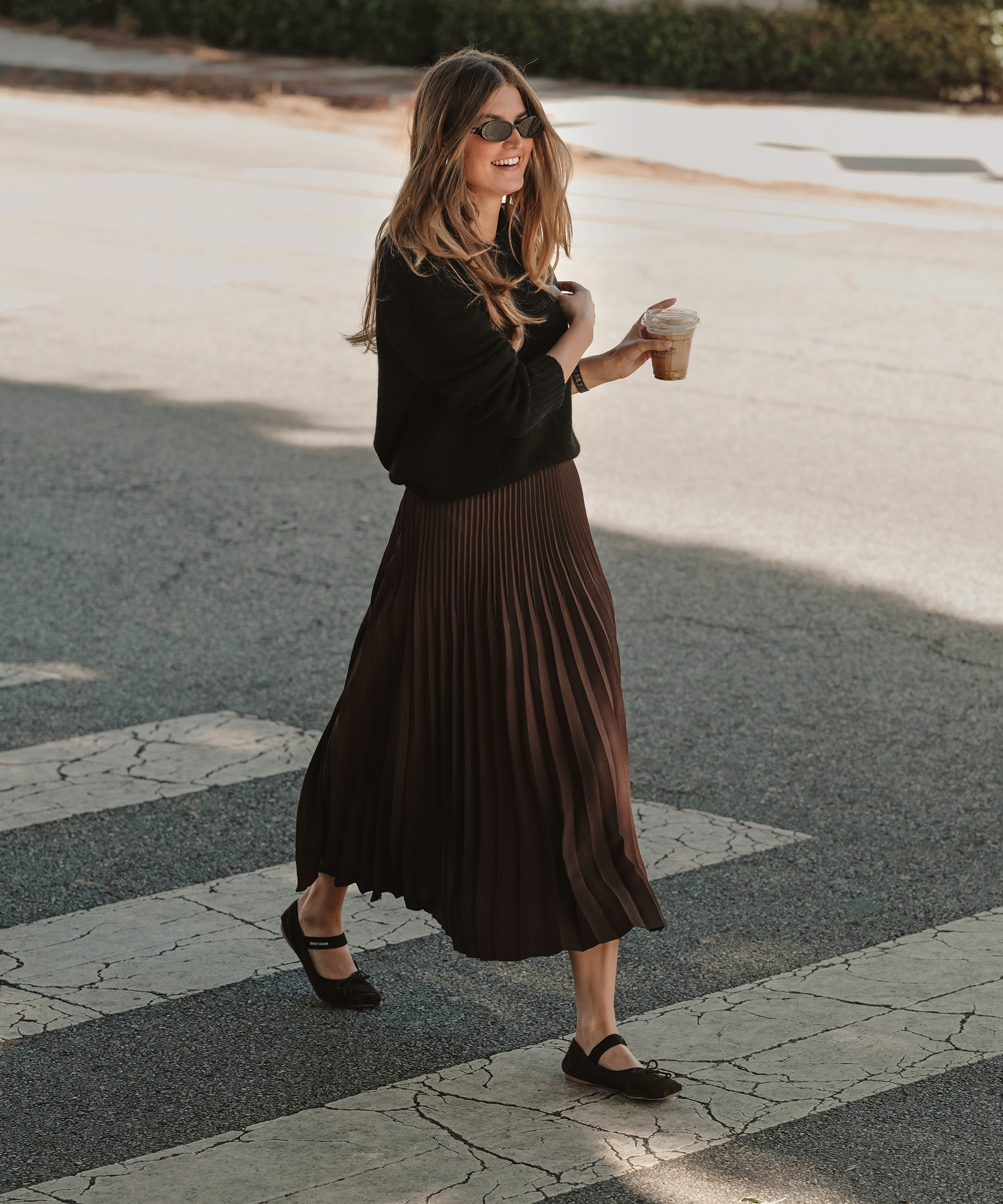 a woman crossing the street wearing a pleated skirt in chocolate and a black cashmere sweater