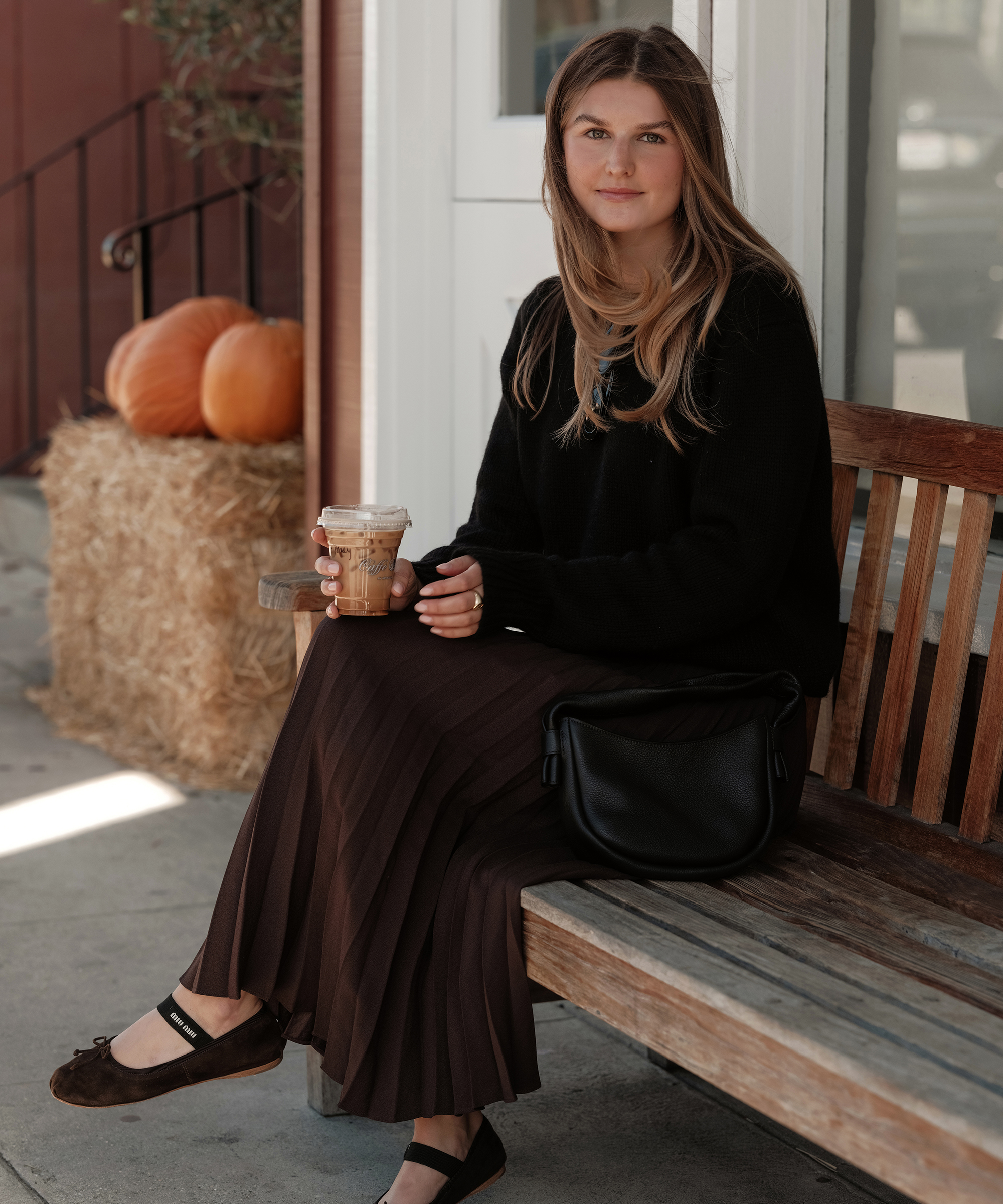 a woman sitting on a bench wearing a chocolate pleated skirt and black cashmere sweater