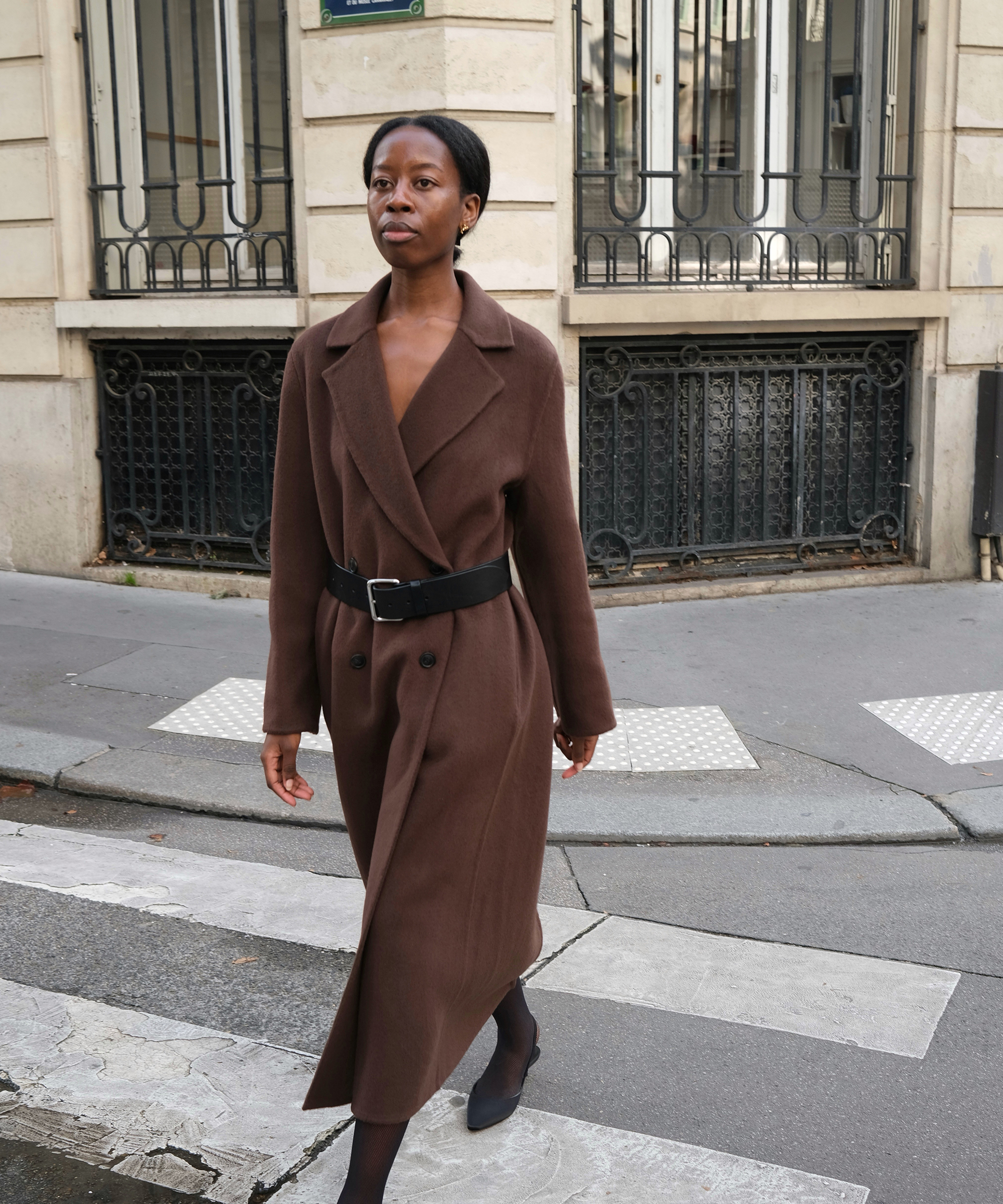 sylvie walking down the street in a chocolate trench coat with satin kitten heels