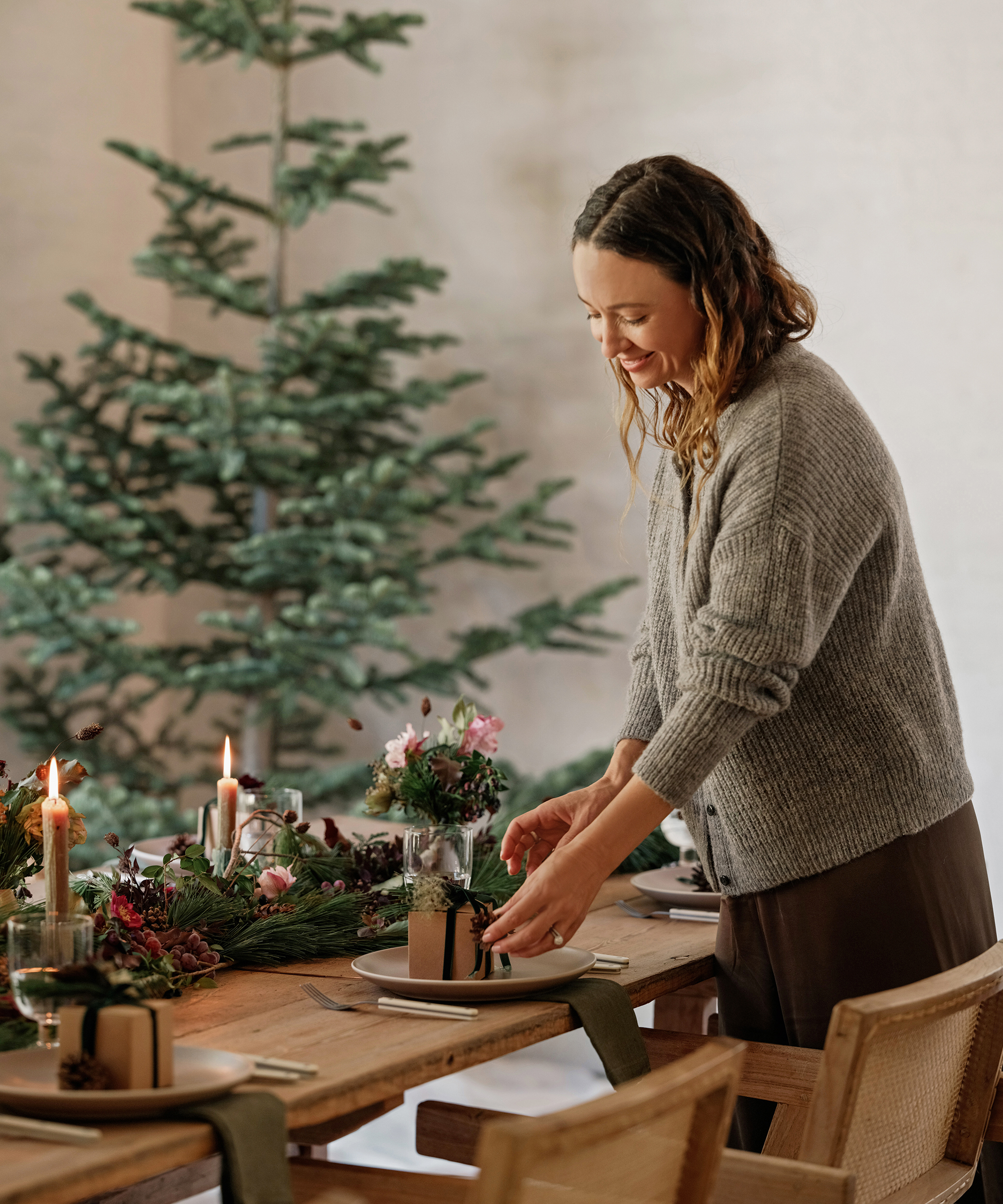 jenni setting a holiday table in a grey hayes crewneck sweater with a christmas tree behind her