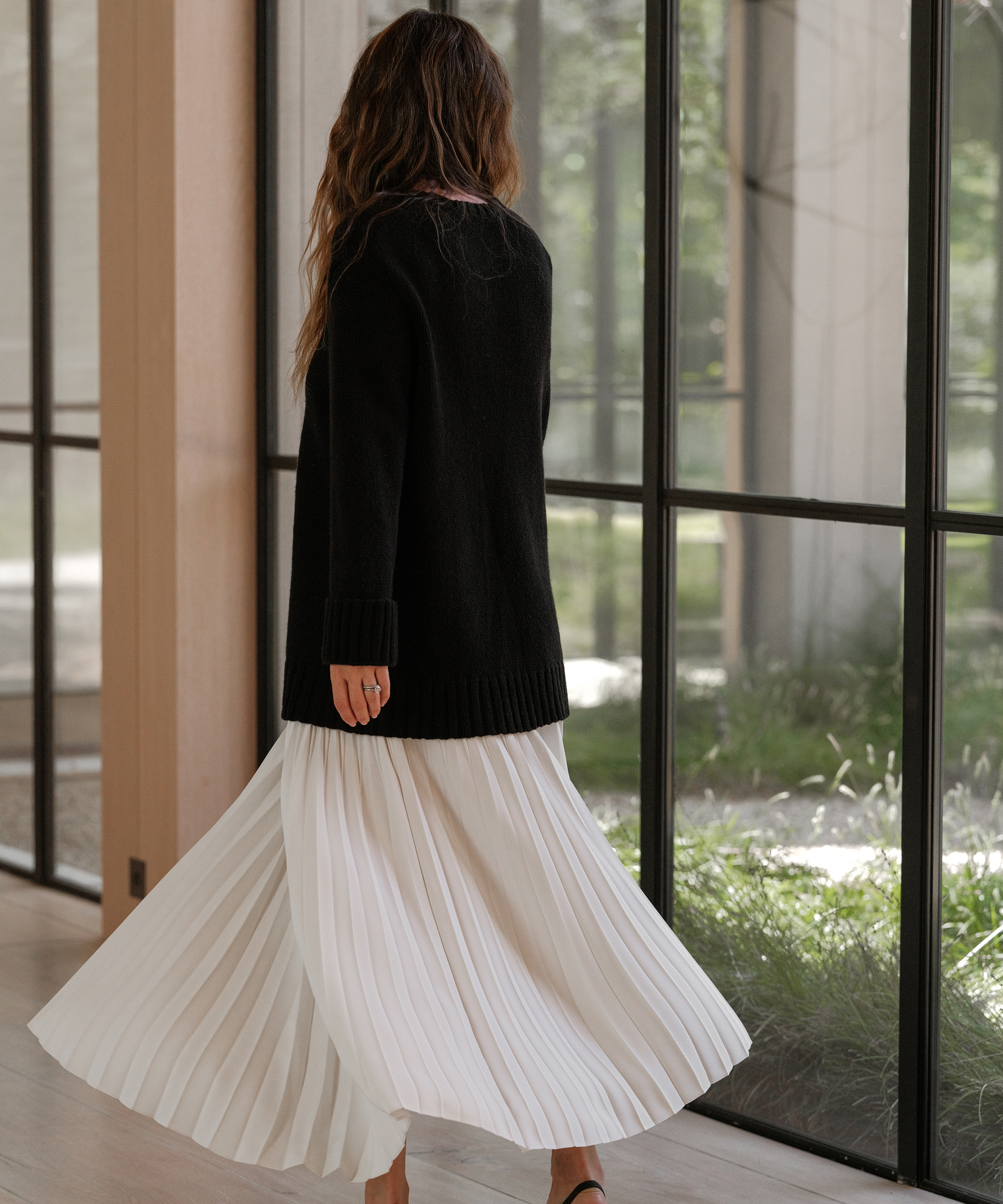 jenni wearing an ivory pleated skirt and black cashmere sweater twirling in a hallway