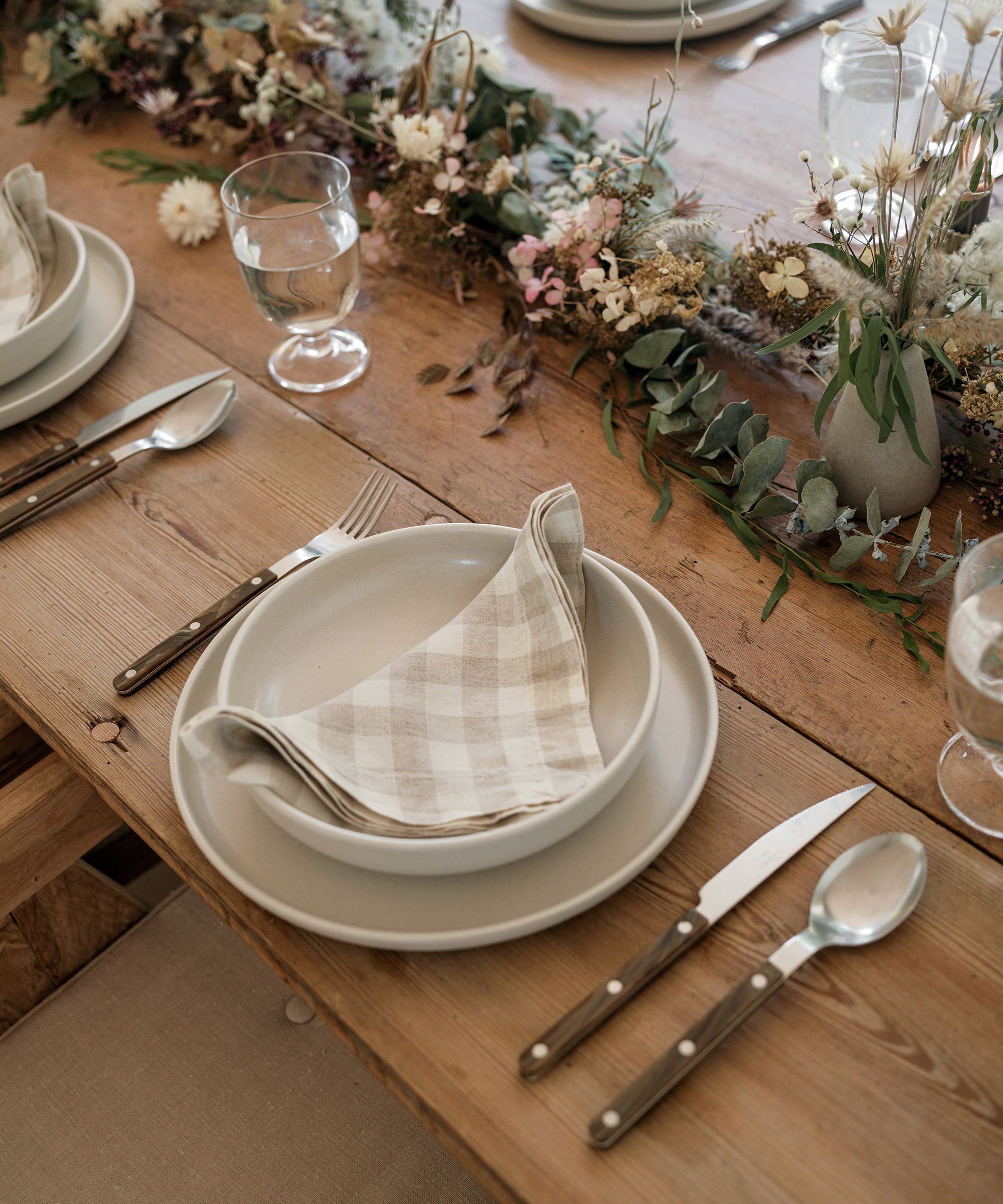 a dinner plate and soup bowl with tortoise cutlery on a wooden dining table with fresh greenery