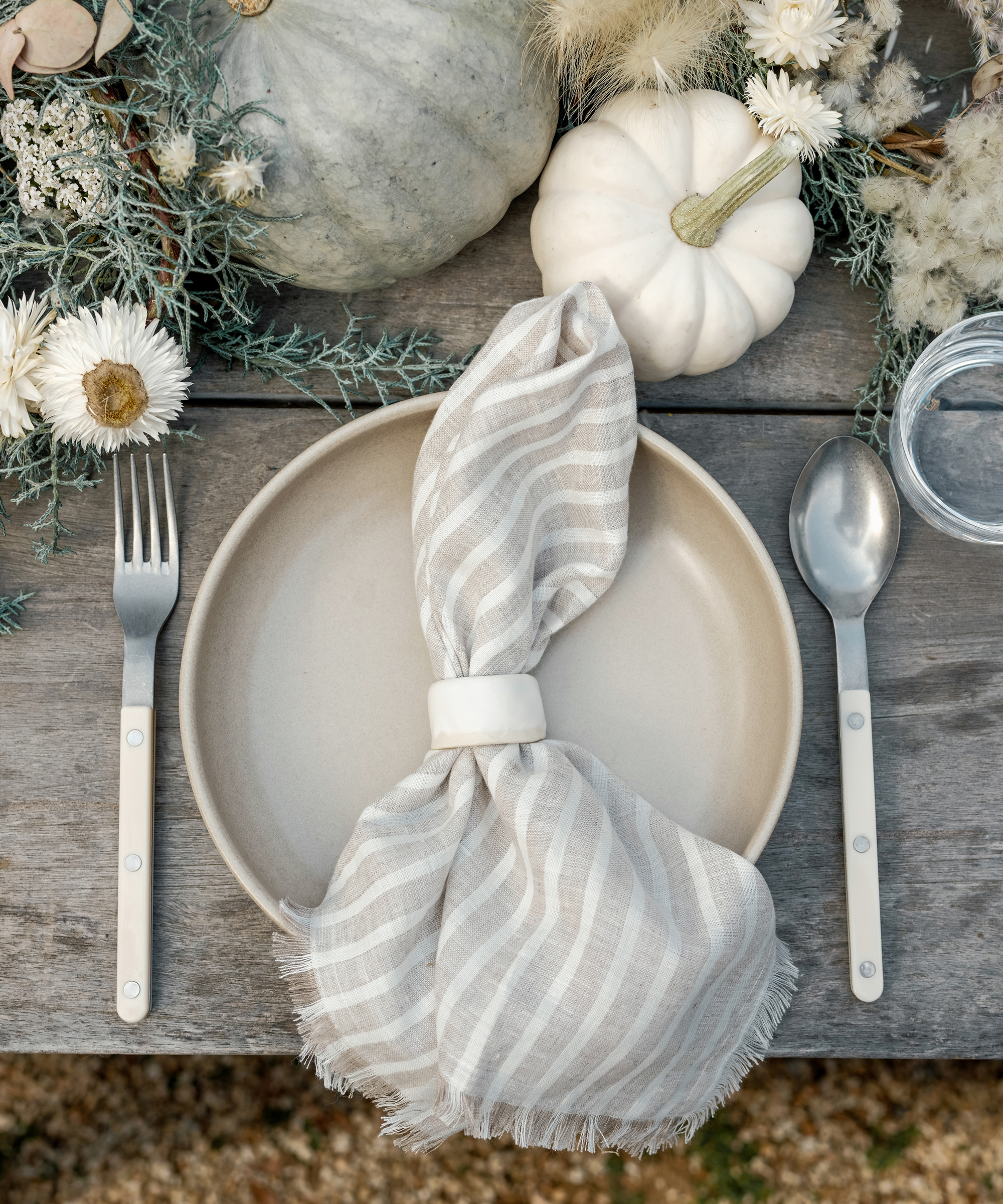 a place setting with a taupe dinner plate and striped linen napkin and ivory cutlerly