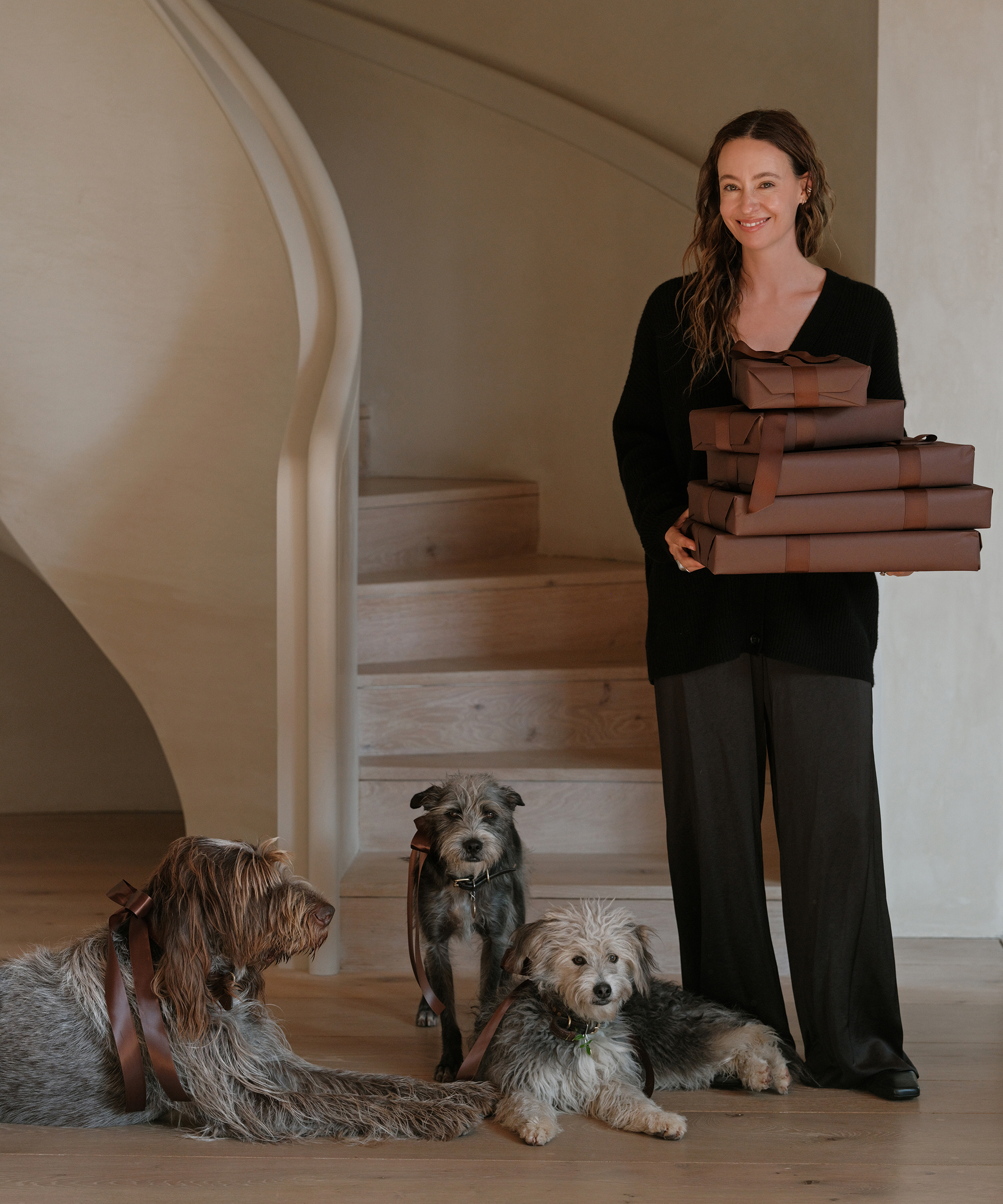 jenni wearing black silk pants and a black cashmere cocoon sweater holding chocolate presents next to her three dogs
