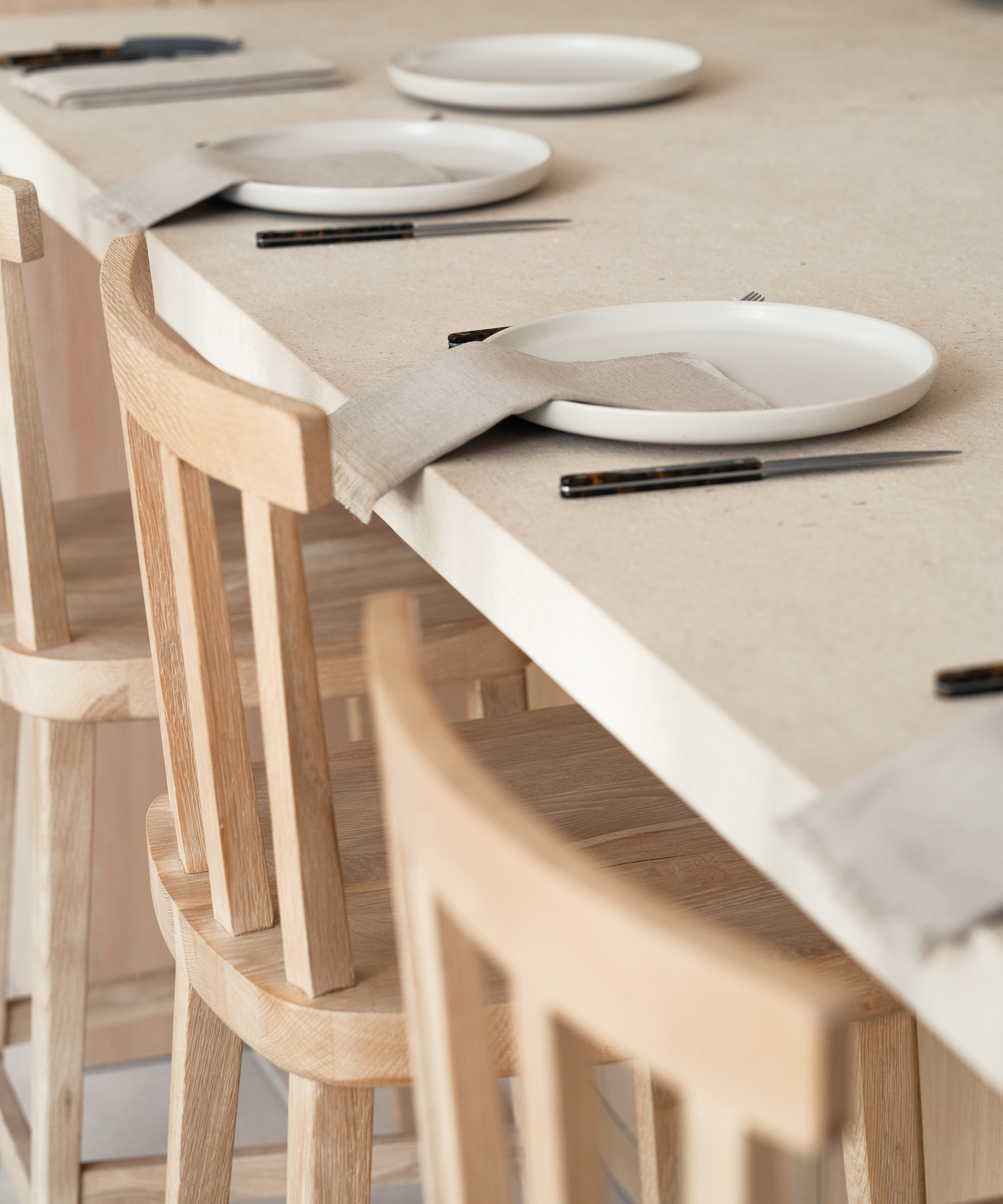 a kitchen counter with taupe dinner plates and a linen napkin with dark cutlery