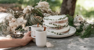 a layered cake with sprigs on an outdoor wooden dining table and two pacific mugs