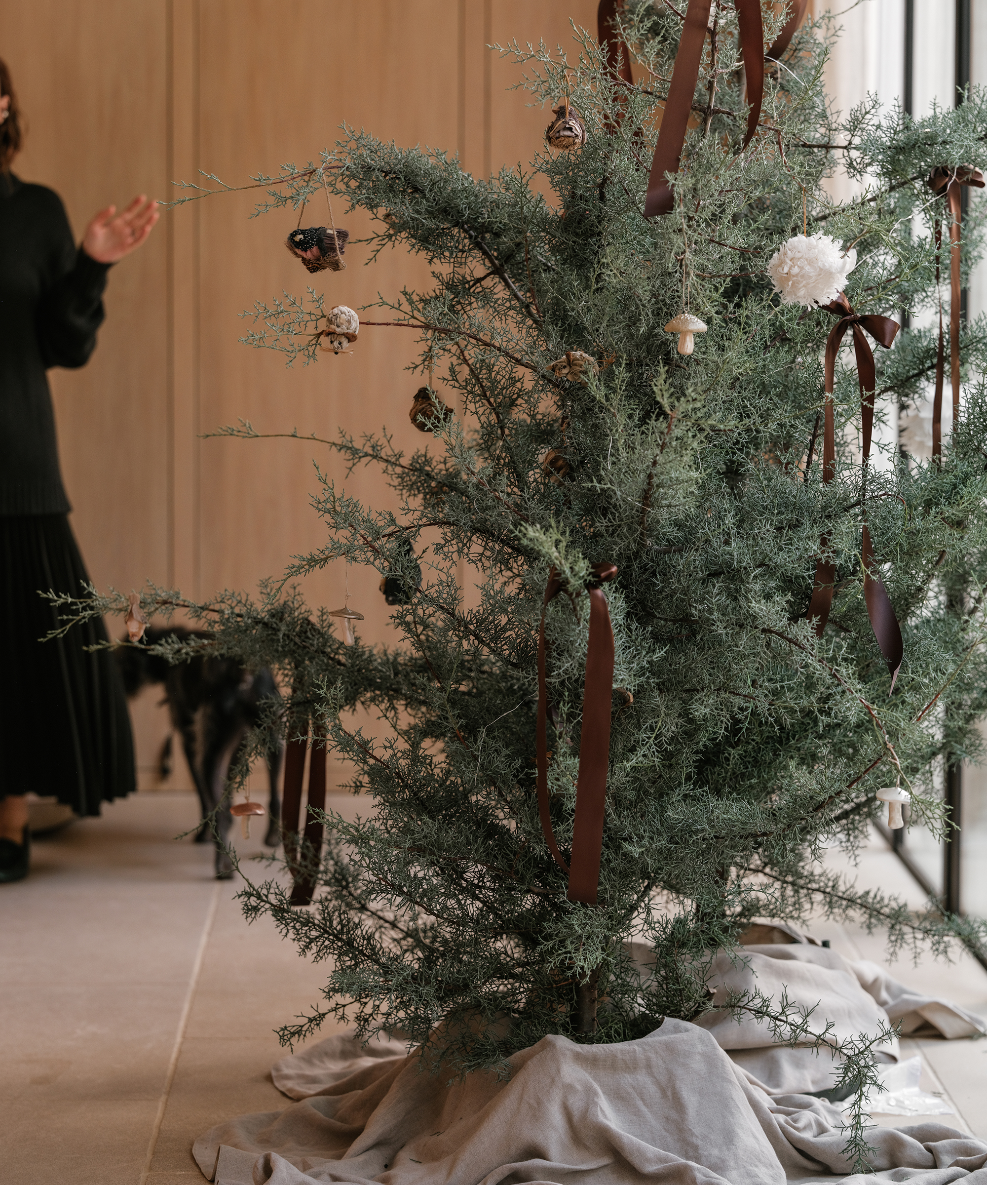 a christmas tree decorated with ornaments and linen taupe tree skirt