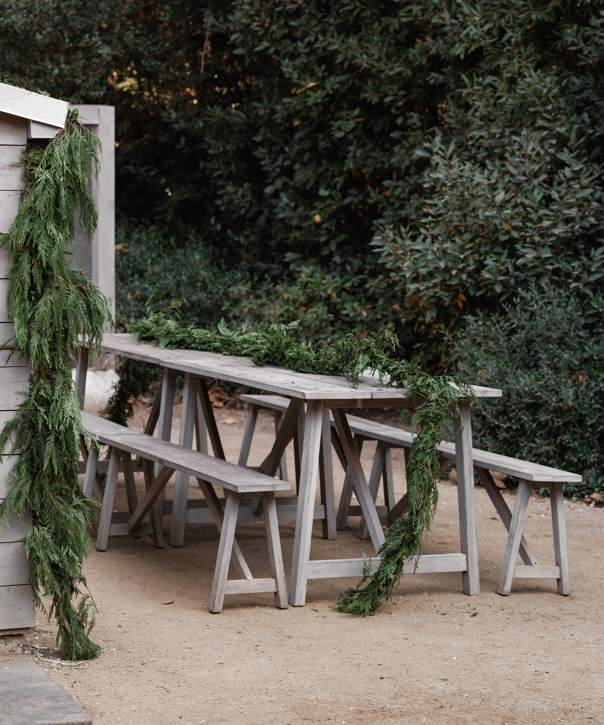 a wooden outdoor dining table with green garland down the middle