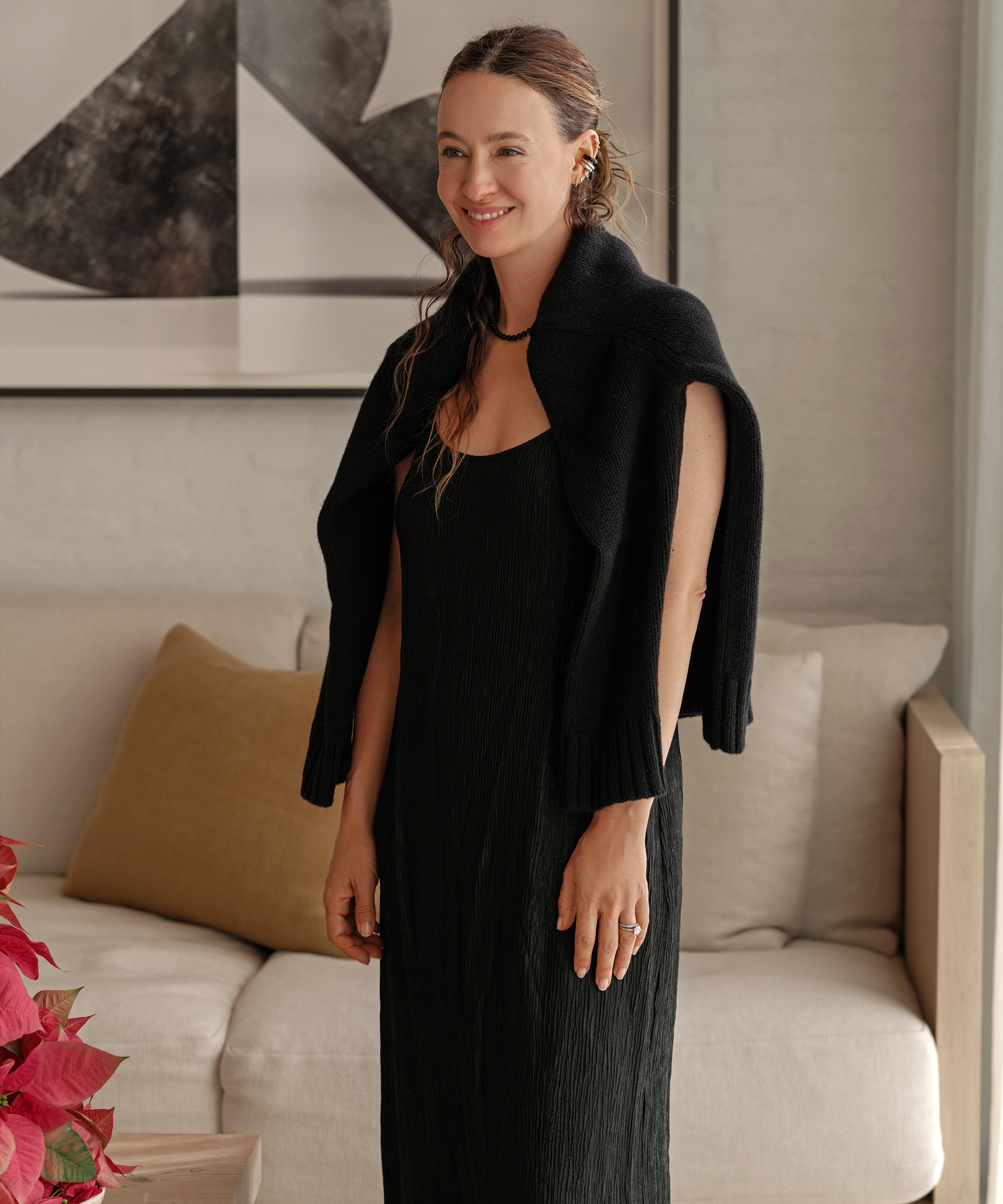 jenni wearing a black dress with a black cashmere sweater over her shoulders standing in the family room