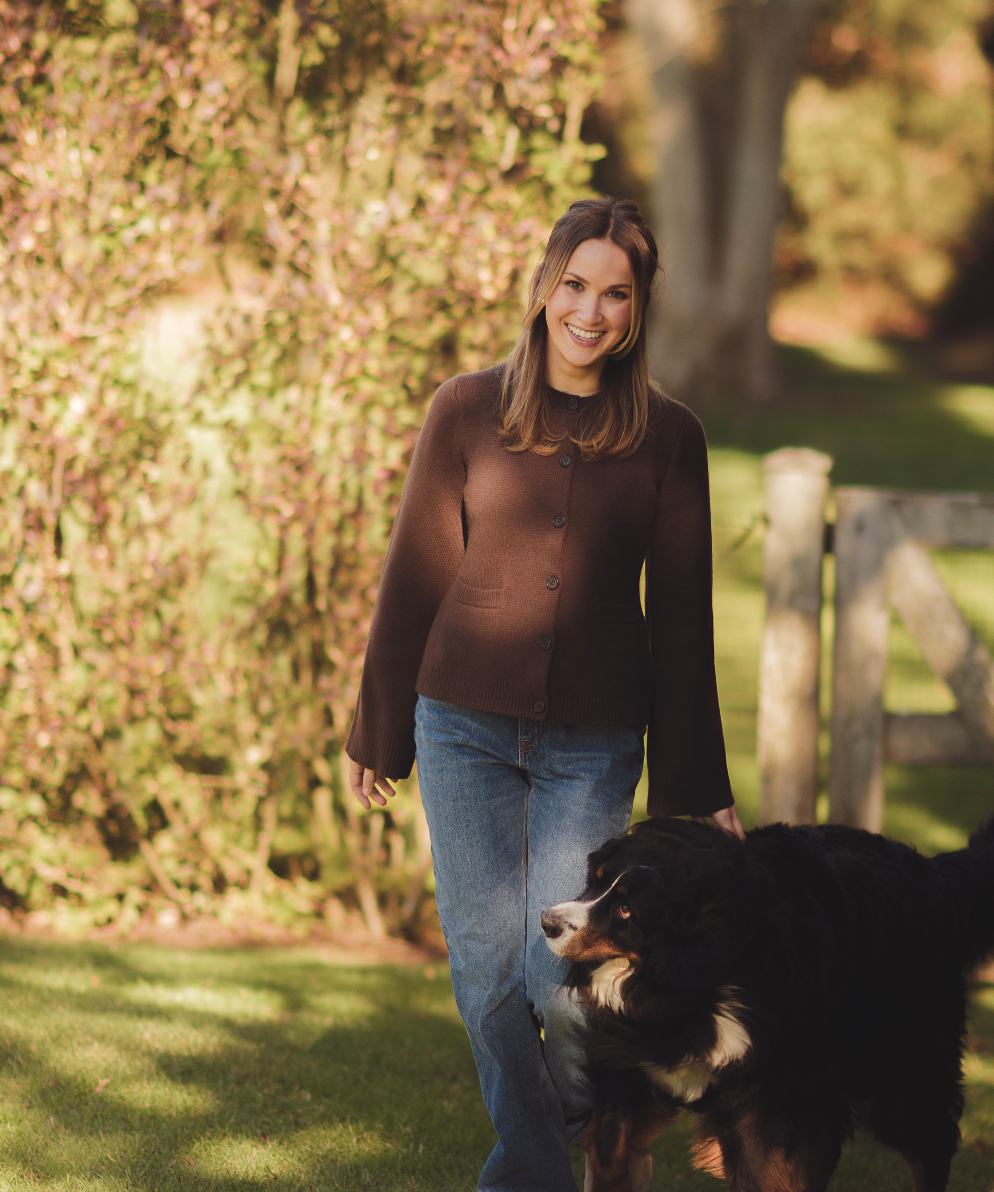 meredith standing outside in a chcolate cooper cardigan with her Bernese mountain dog