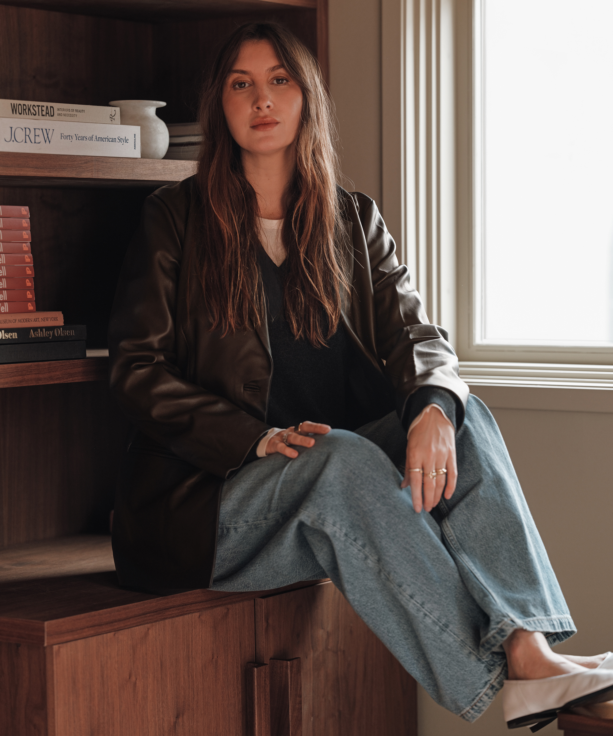 allison wearing a blazer and denim sitting on a wooden ledge